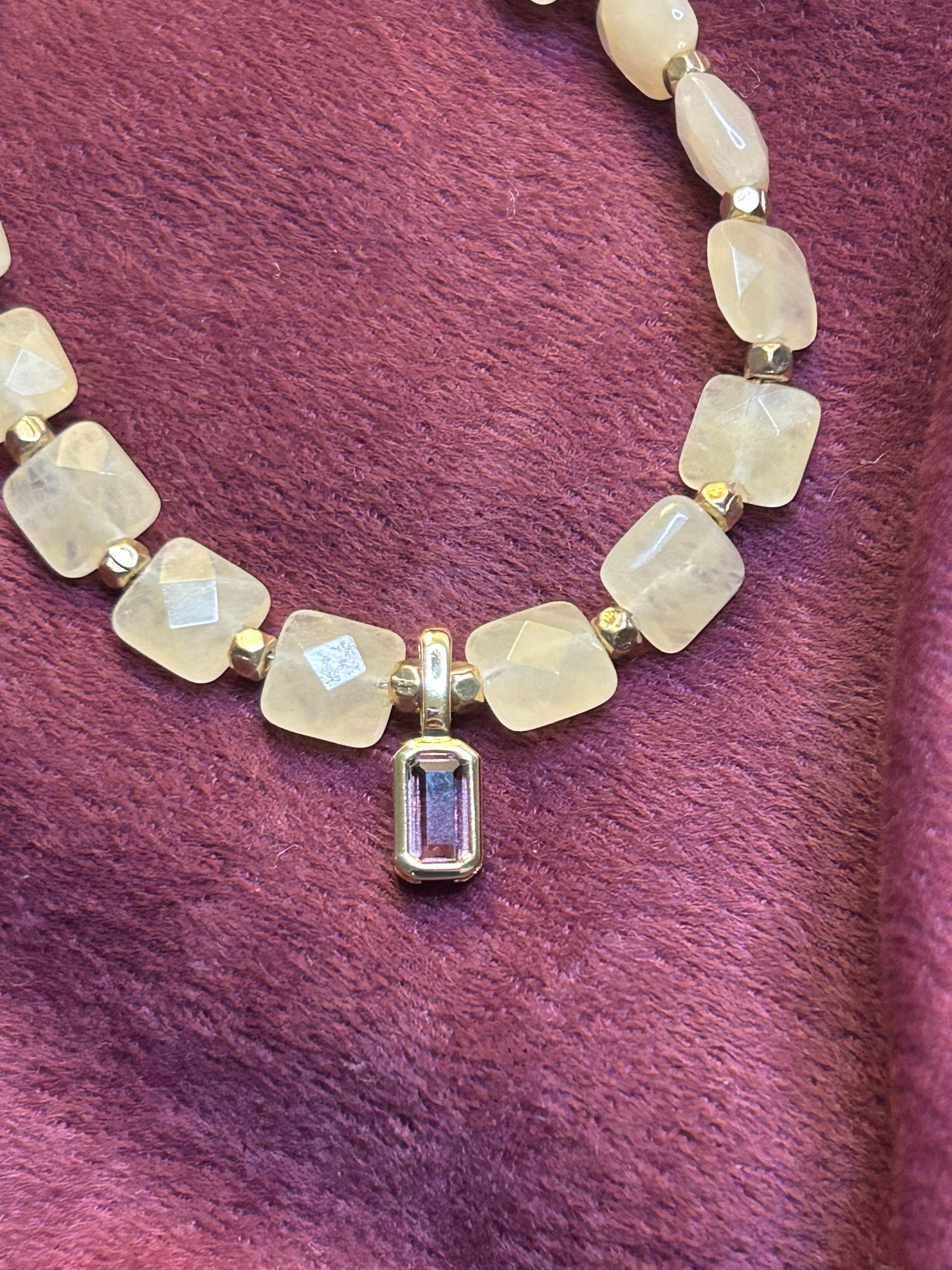 Necklace with light-colored beads and a purple gemstone on a purple fabric background