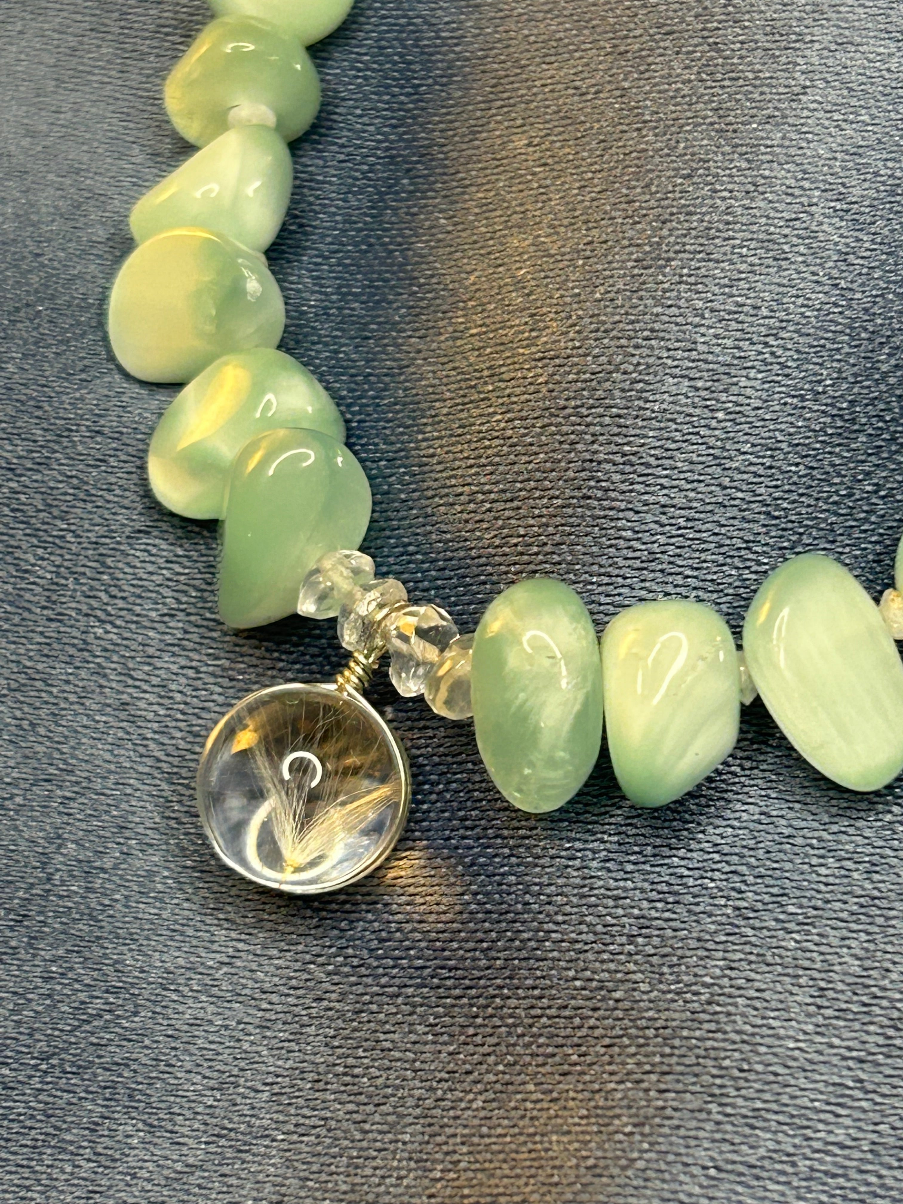 Necklace with green beads and a silver clasp on a gray fabric background