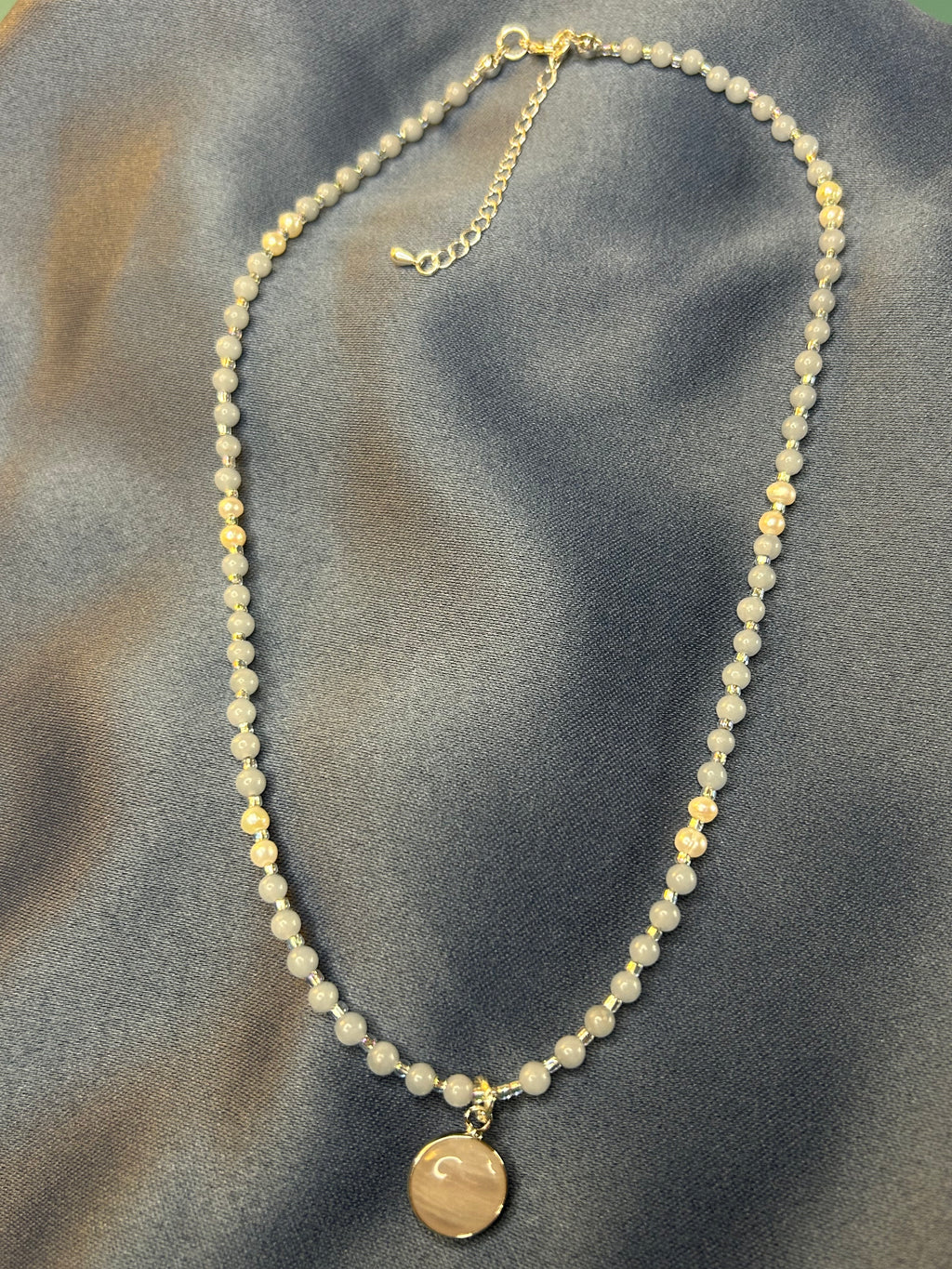 Necklace with round beads and a circular pendant on a textured gray surface