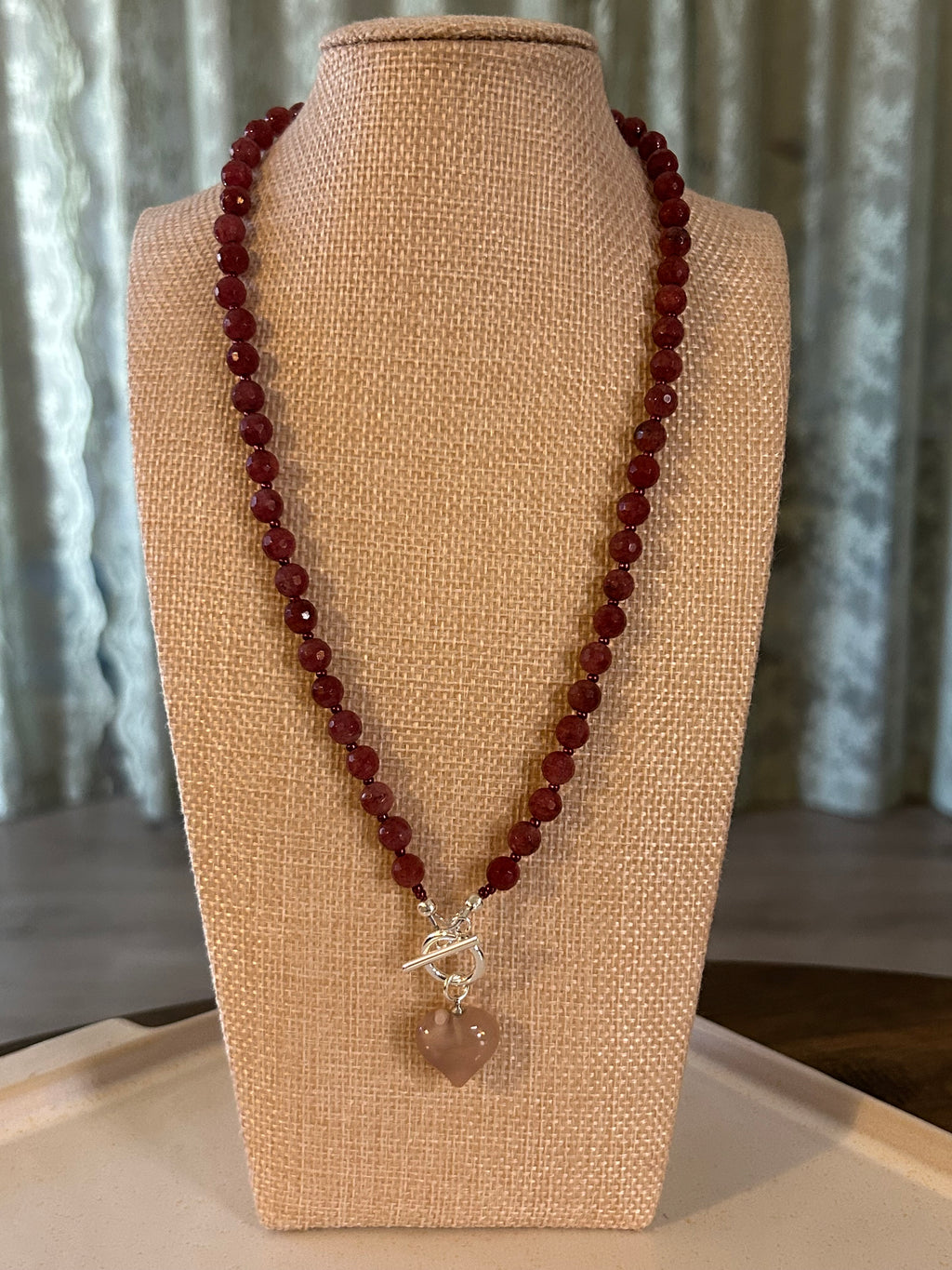 Red beaded necklace with a silver clasp on a beige display stand.