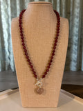 Red beaded necklace with a silver clasp on a beige display stand.