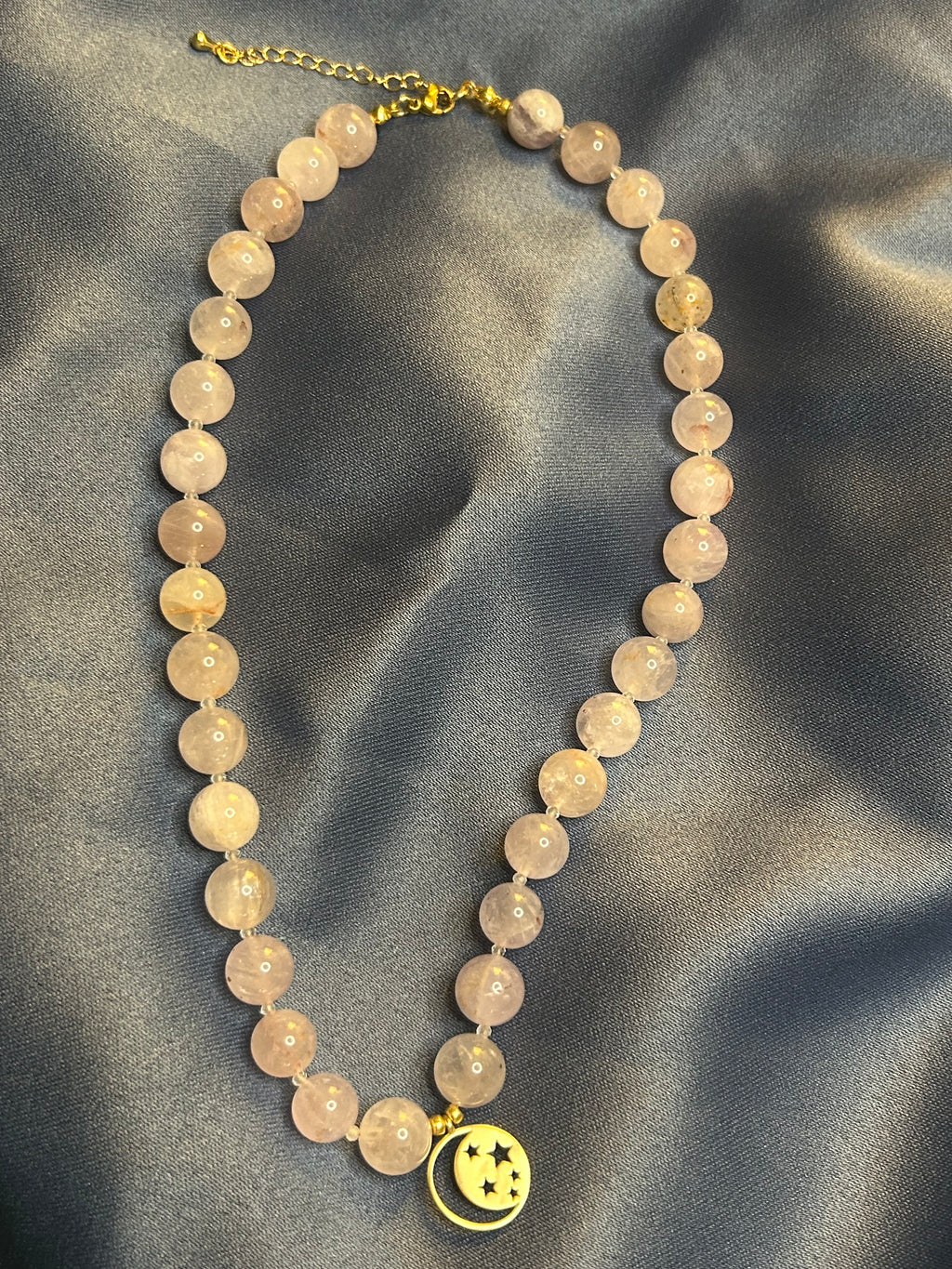 Necklace with pu7 beads and a gold charm on a gray fabric background