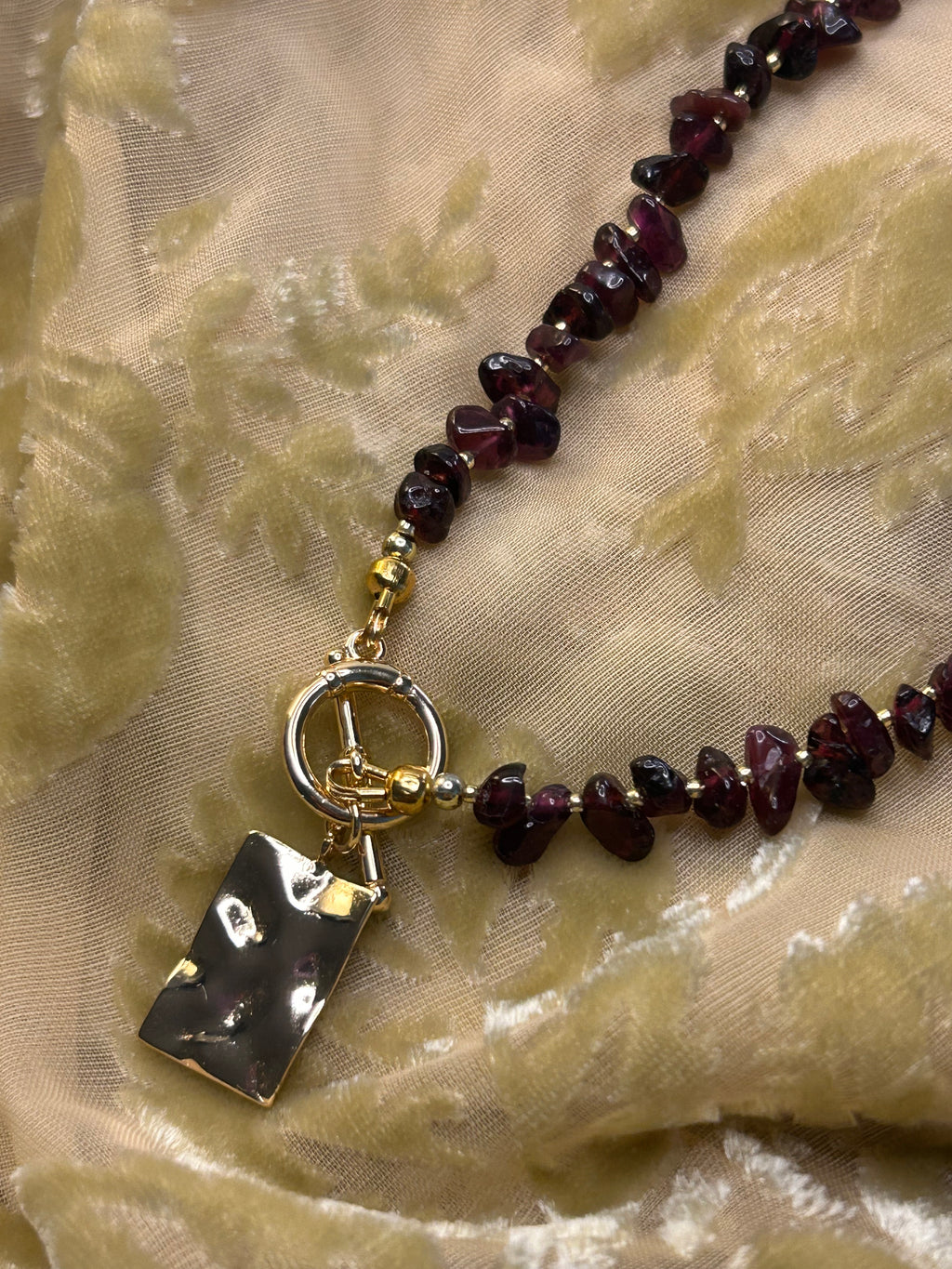 Necklace with dark beads and a black rectangular pendant on a textured beige fabric background