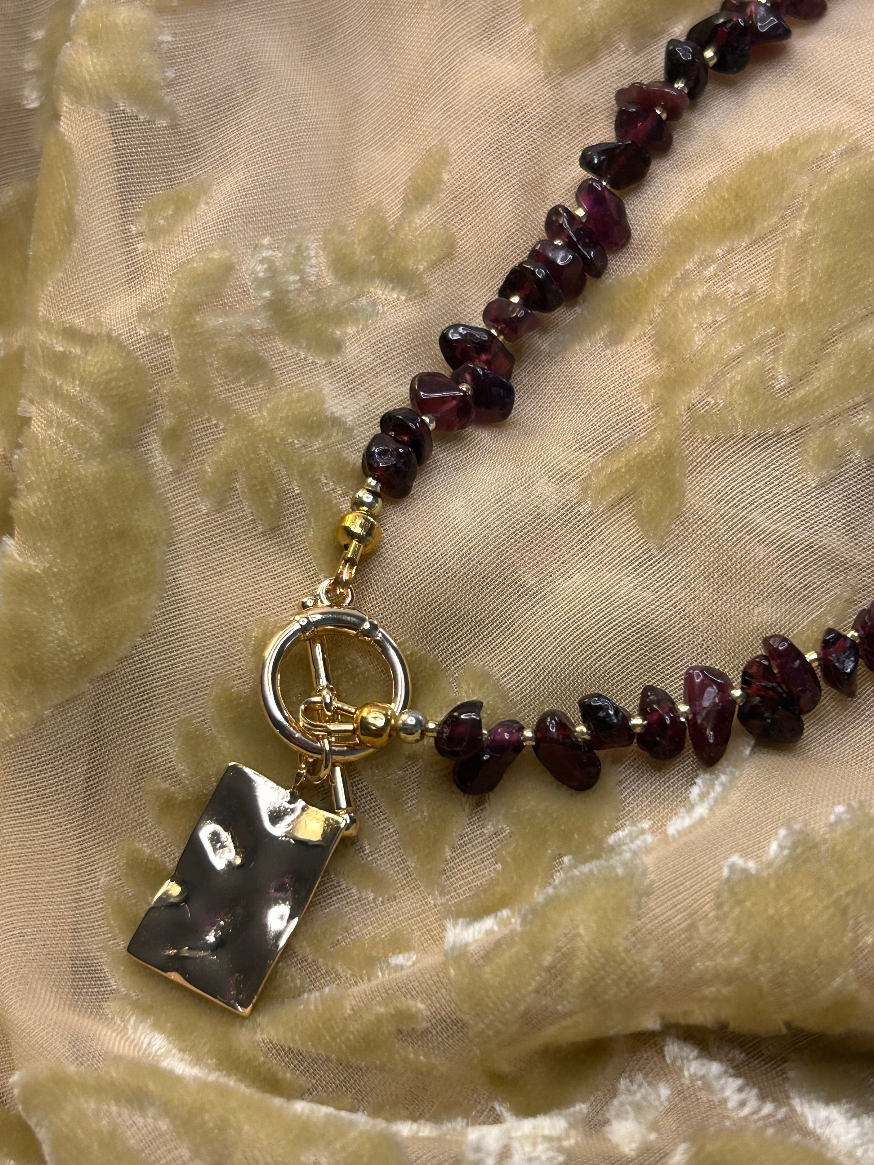 Necklace with dark beads and a black rectangular pendant on a textured beige fabric background