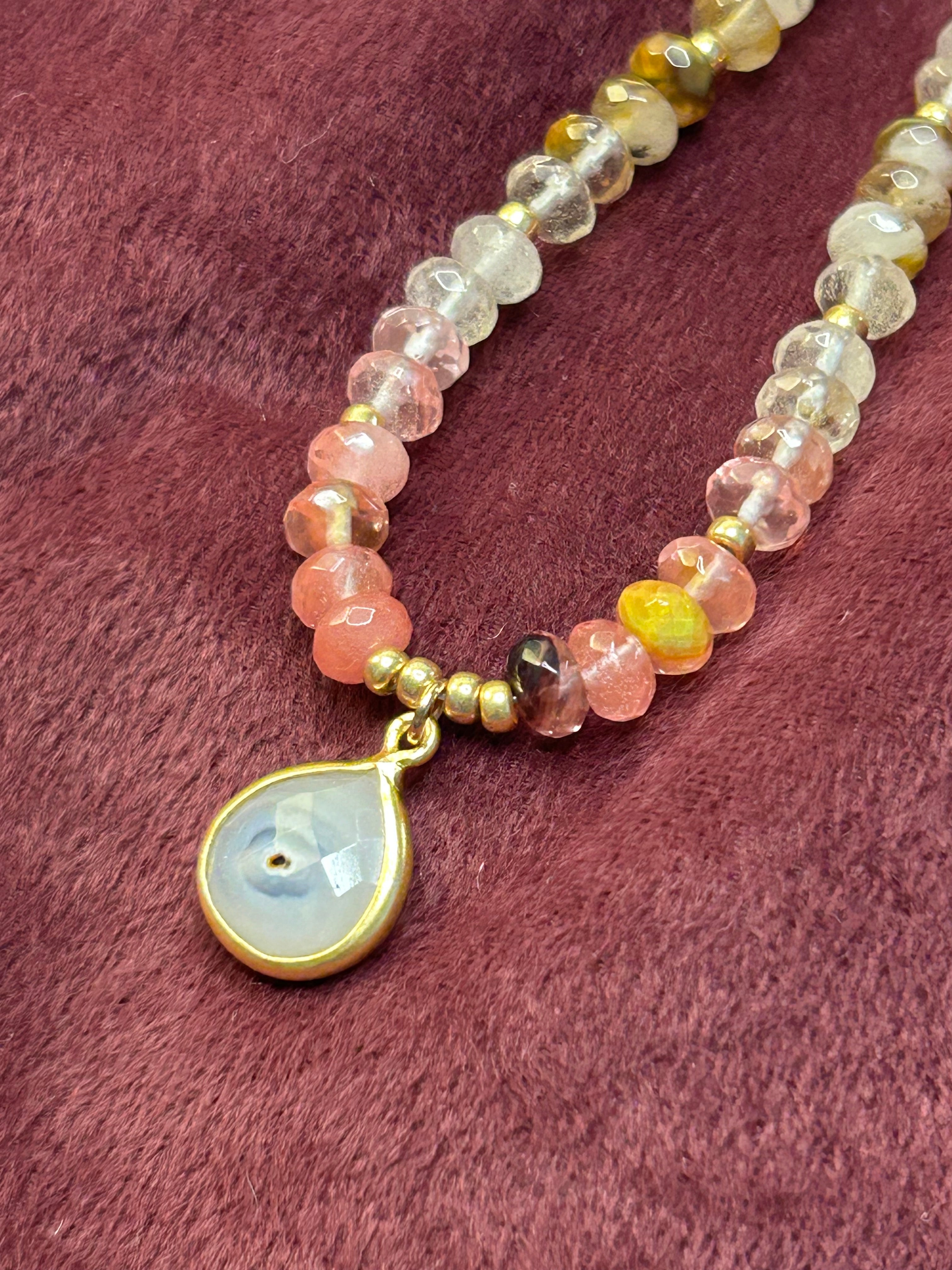 Beaded necklace with a teardrop-shaped pendant on a textured pink surface