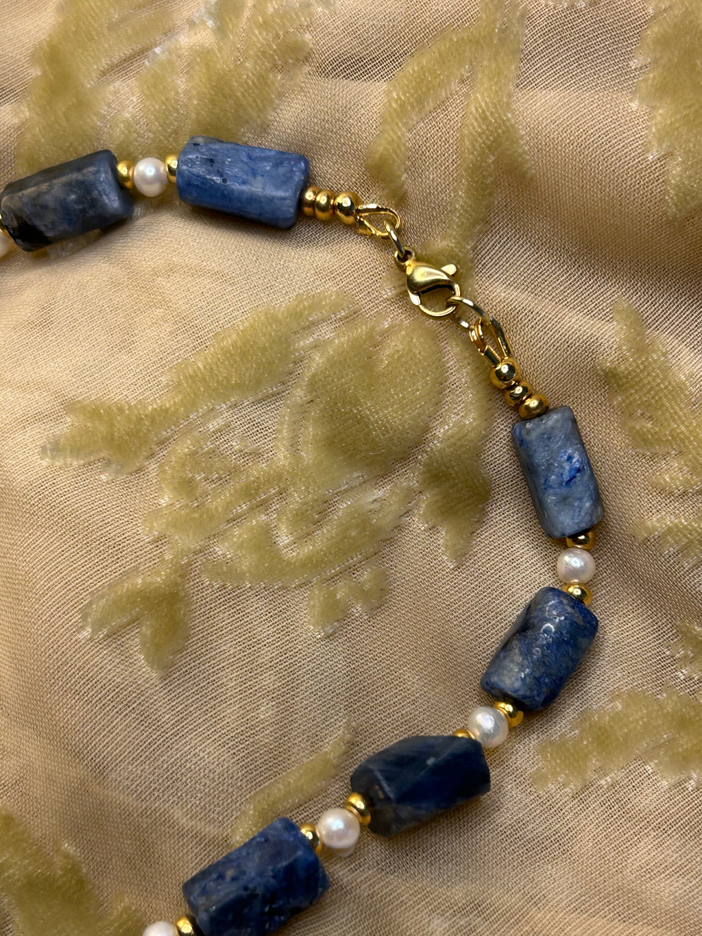 Bracelet with blue beads and gold chain on a textured beige background