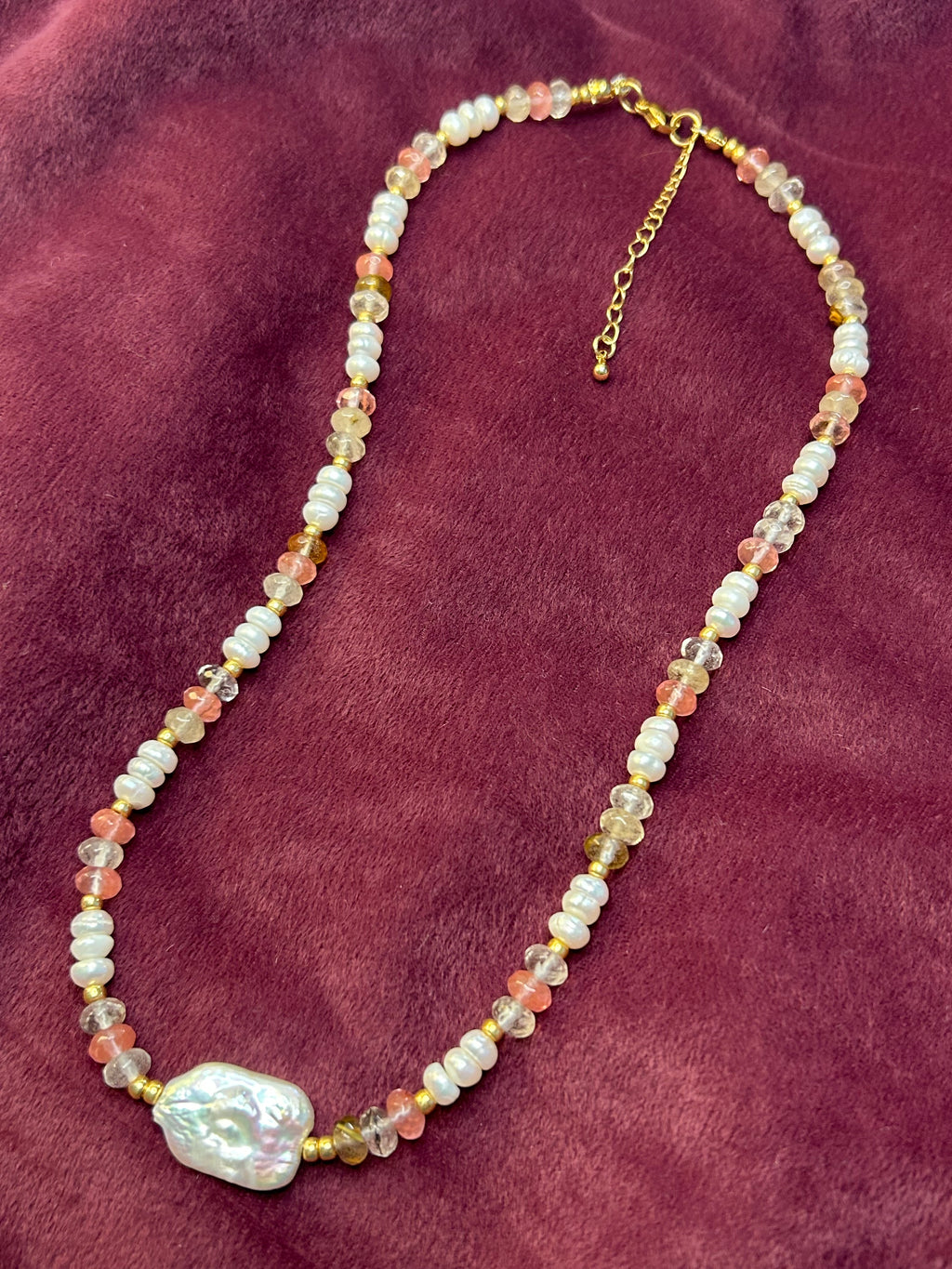 Beaded necklace with a large pearl on a maroon fabric background