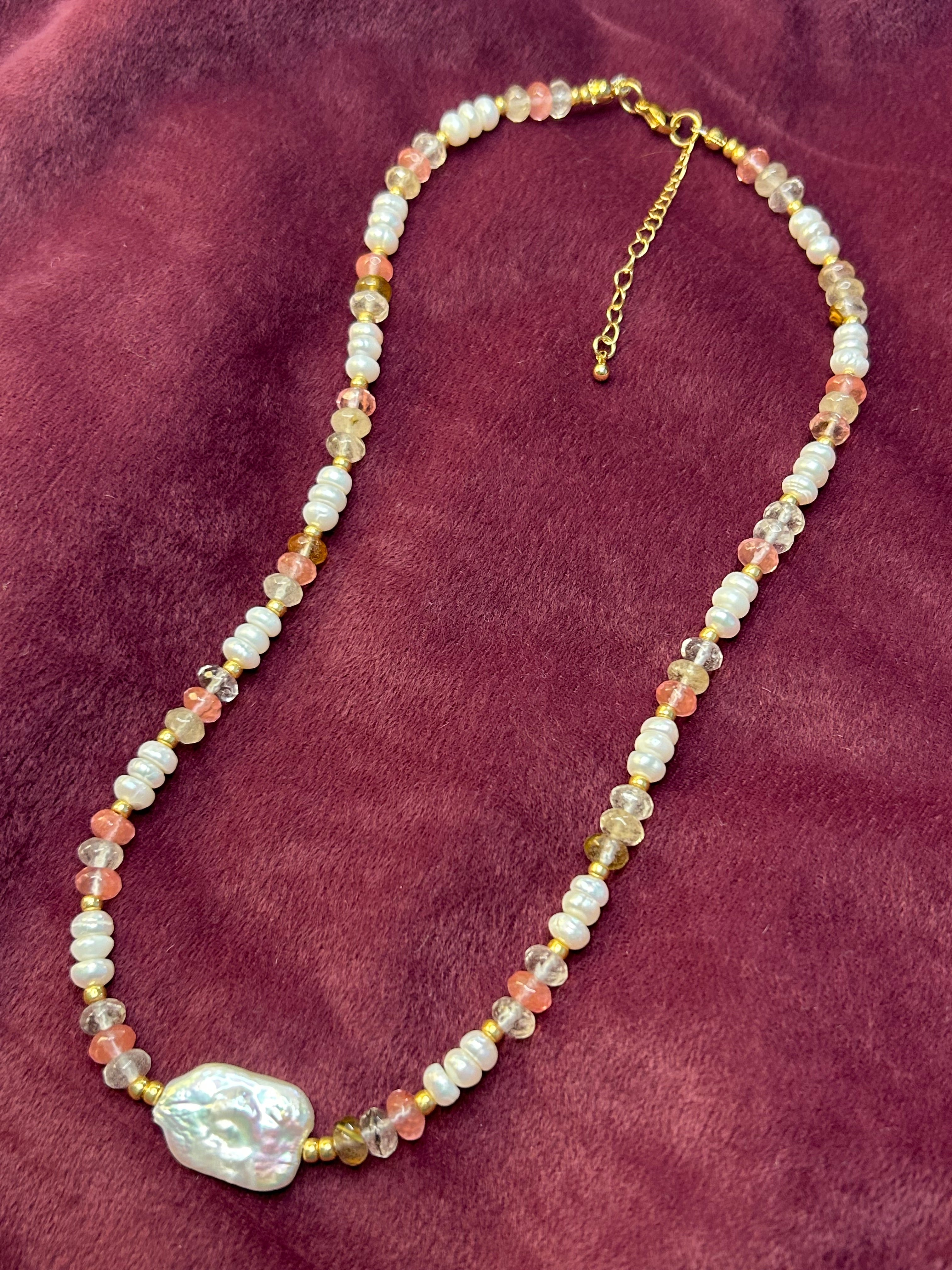 Beaded necklace with a large pearl on a maroon fabric background
