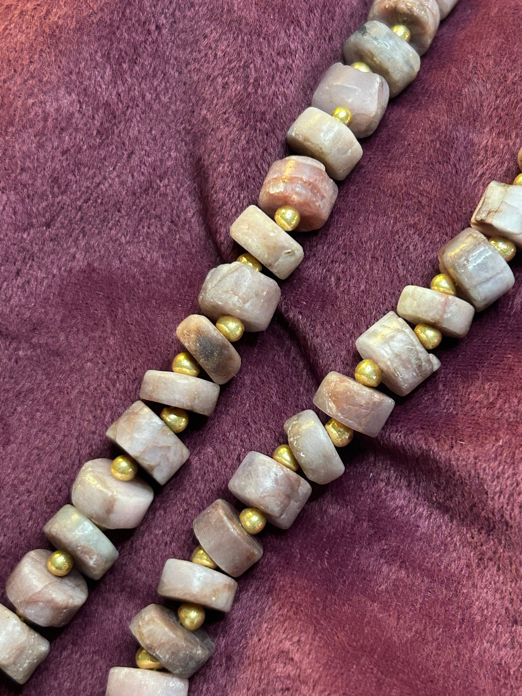 Necklace with pink stones and gold beads on a purple fabric background