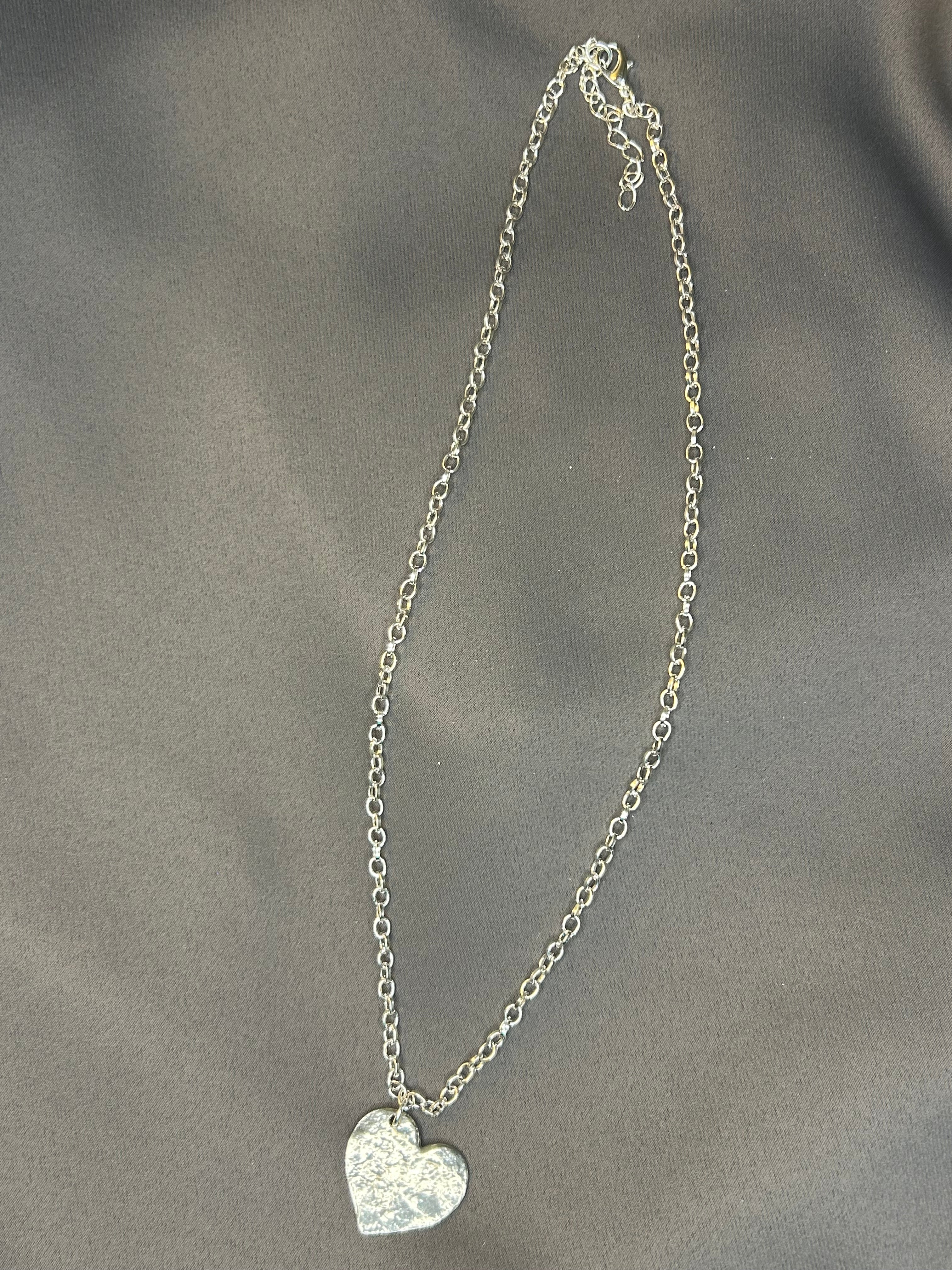 Silver heart-shaped pendant on a chain against a gray background