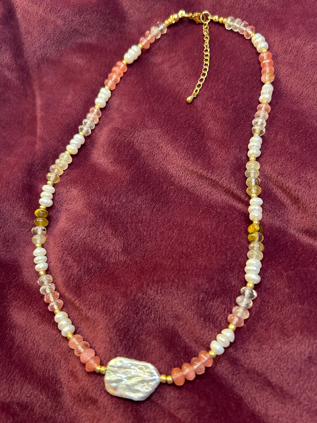 Beaded necklace with a large decorative bead on a maroon fabric background