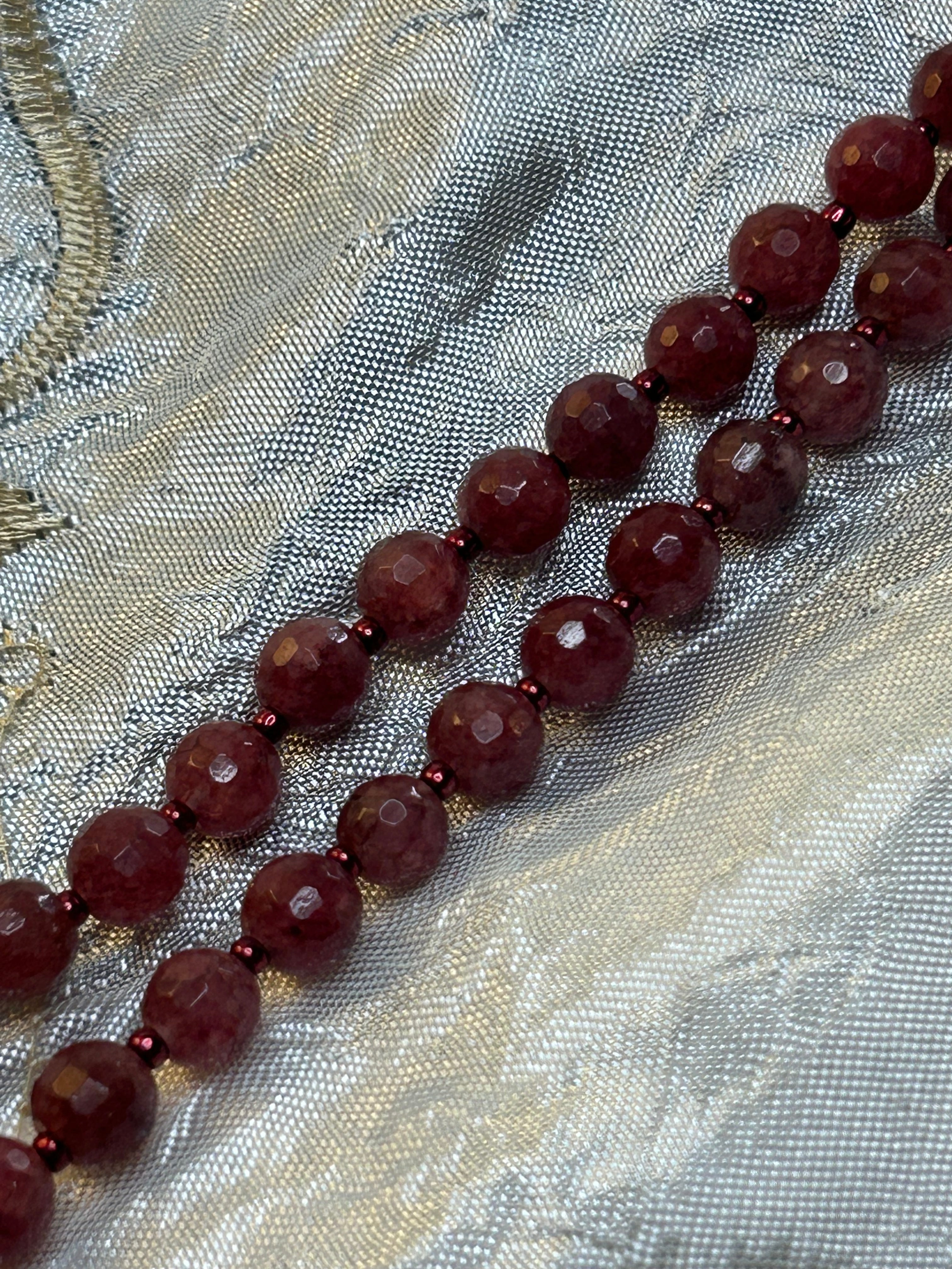 Necklace with dark red beads on a textured fabric background