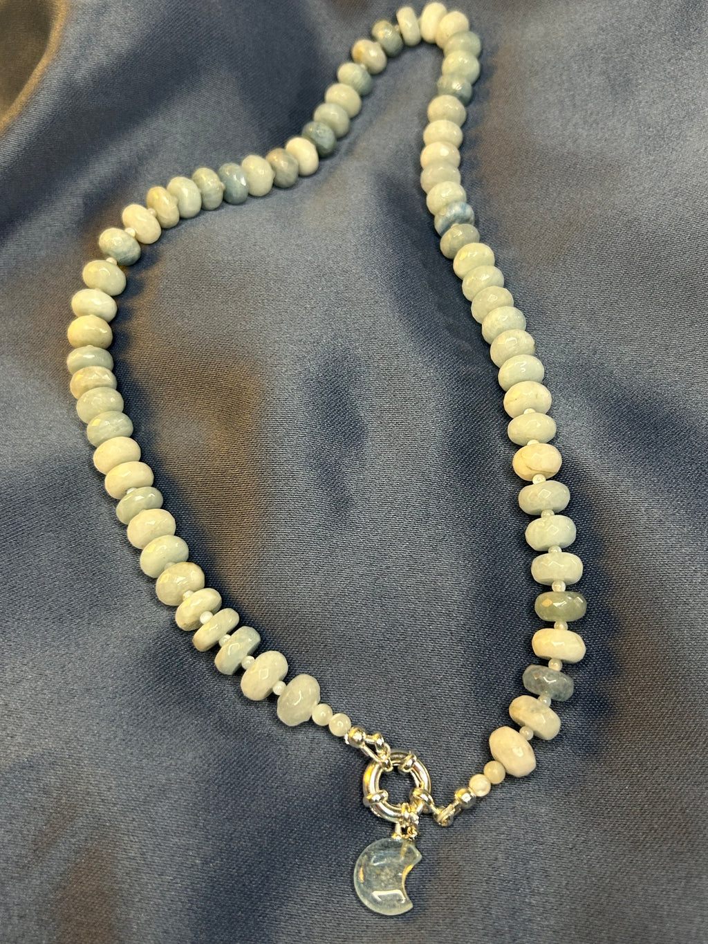 Necklace with light-colored beads and a gold clasp on a gray fabric background