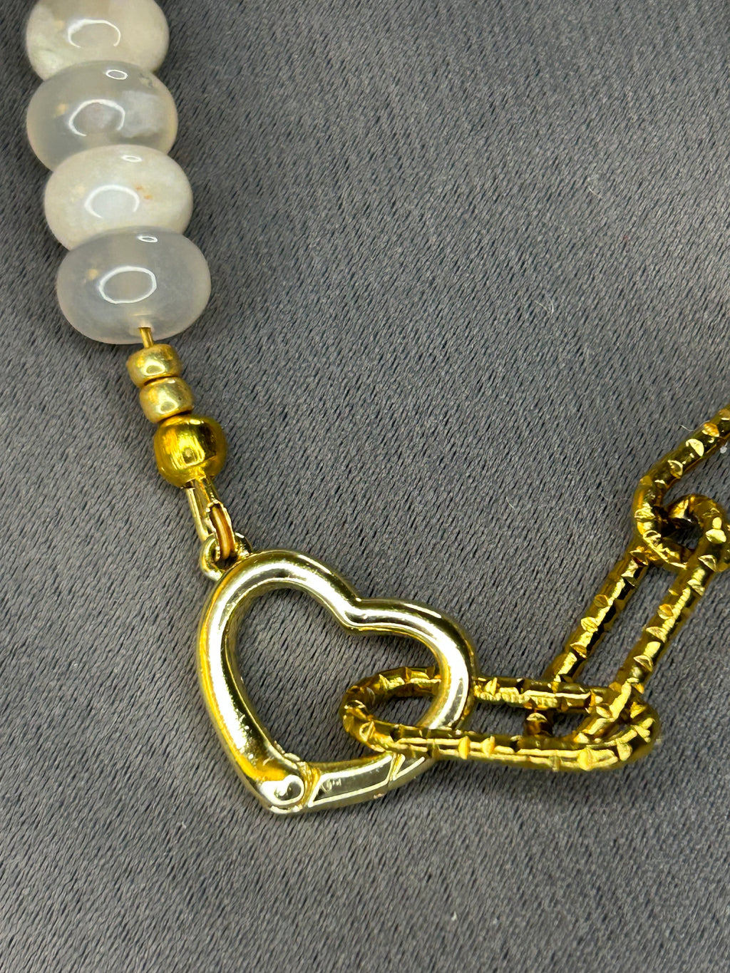 Gold heart charm on a beaded necklace against a gray background