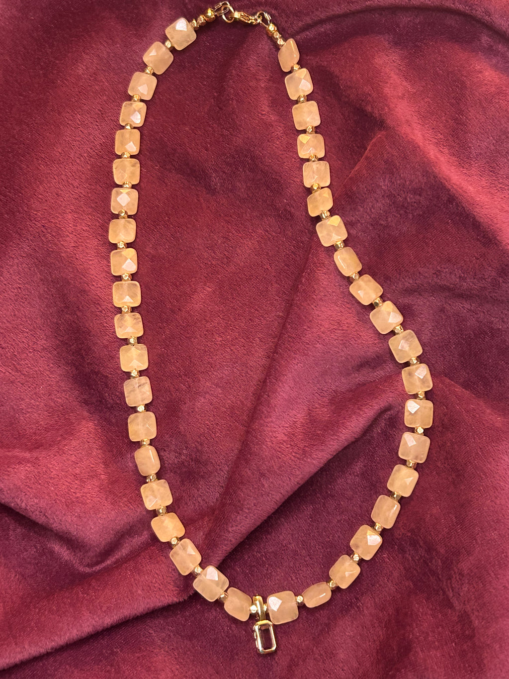 Gold beaded necklace on a maroon fabric background