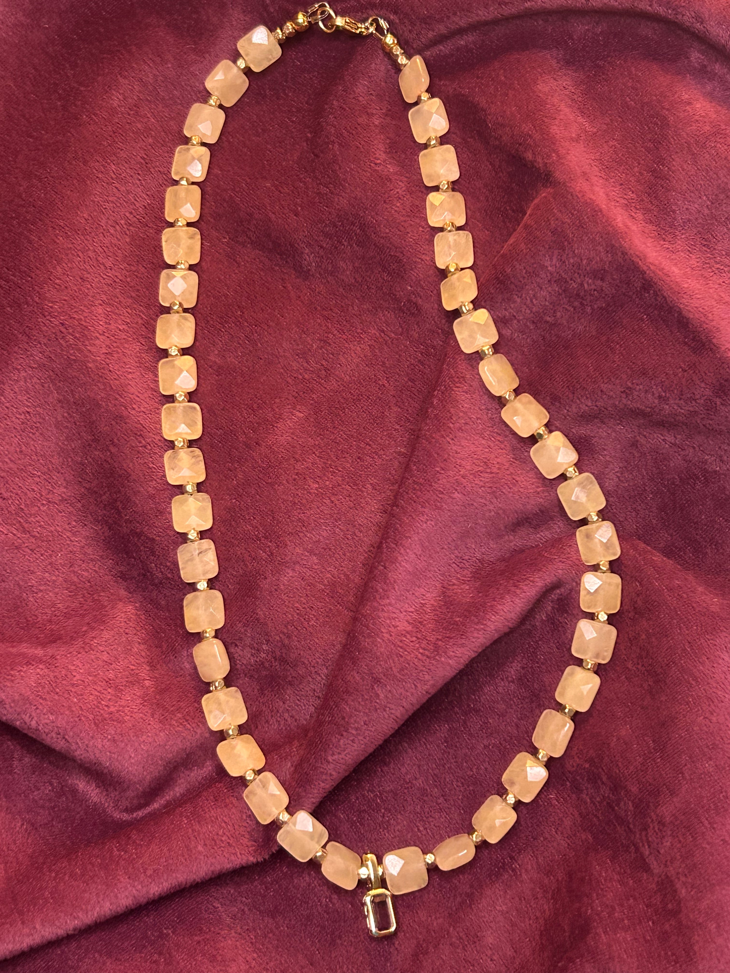 Gold beaded necklace on a maroon fabric background