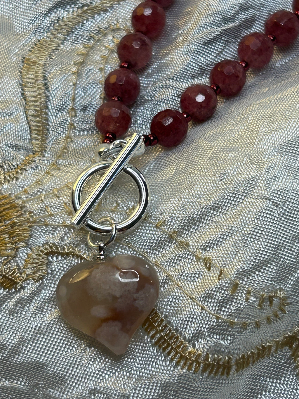 Necklace with red beads and a toggle clasp on a textured fabric background