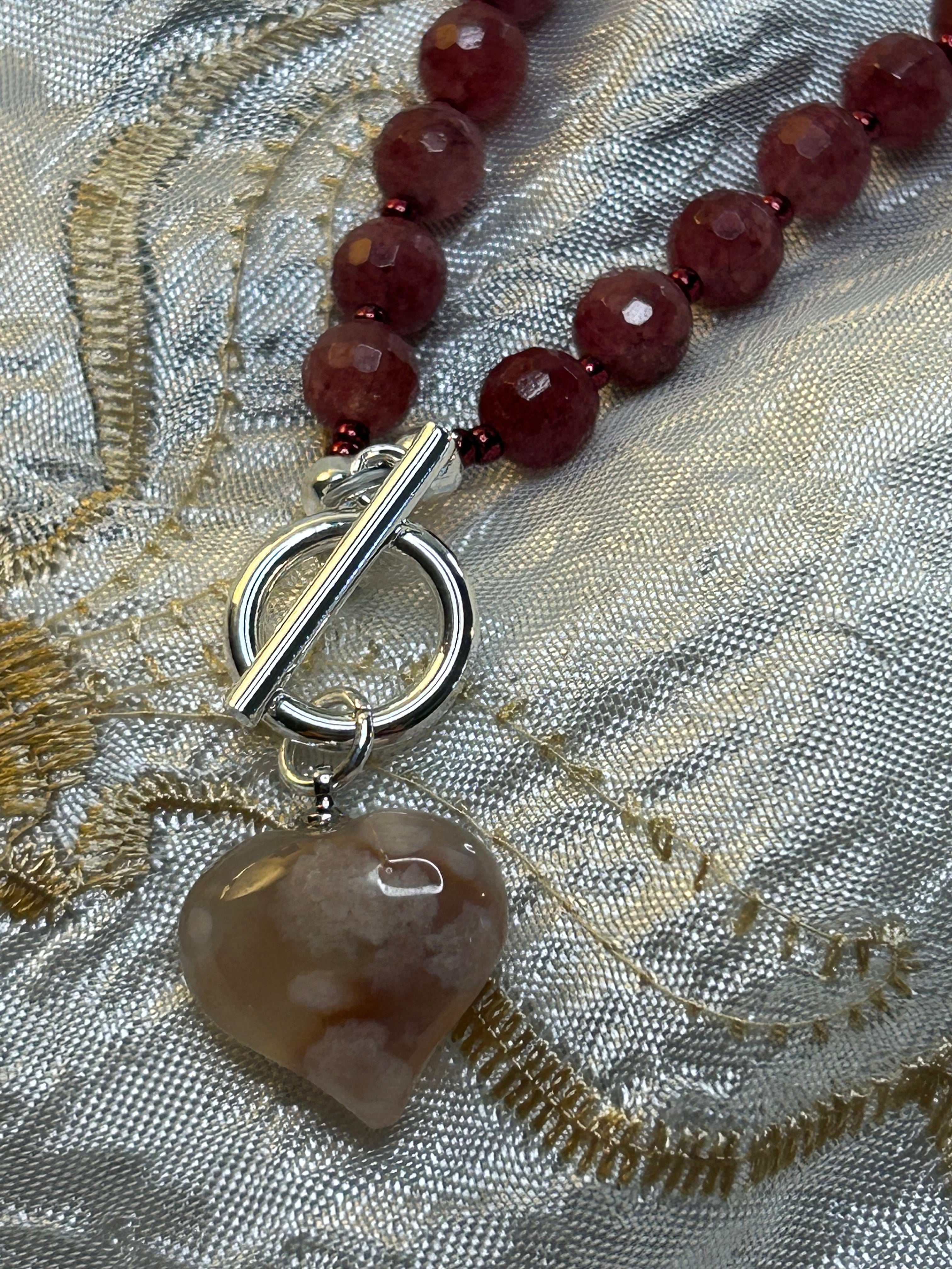 Necklace with red beads and a toggle clasp on a textured fabric background