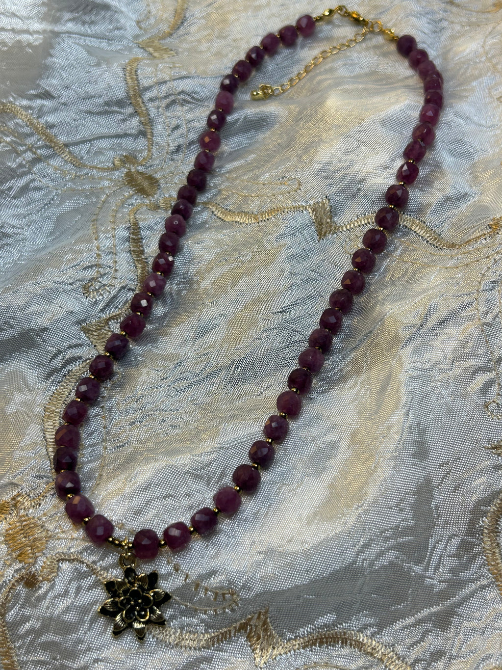 Purple beaded necklace with a gold chain on a textured fabric background