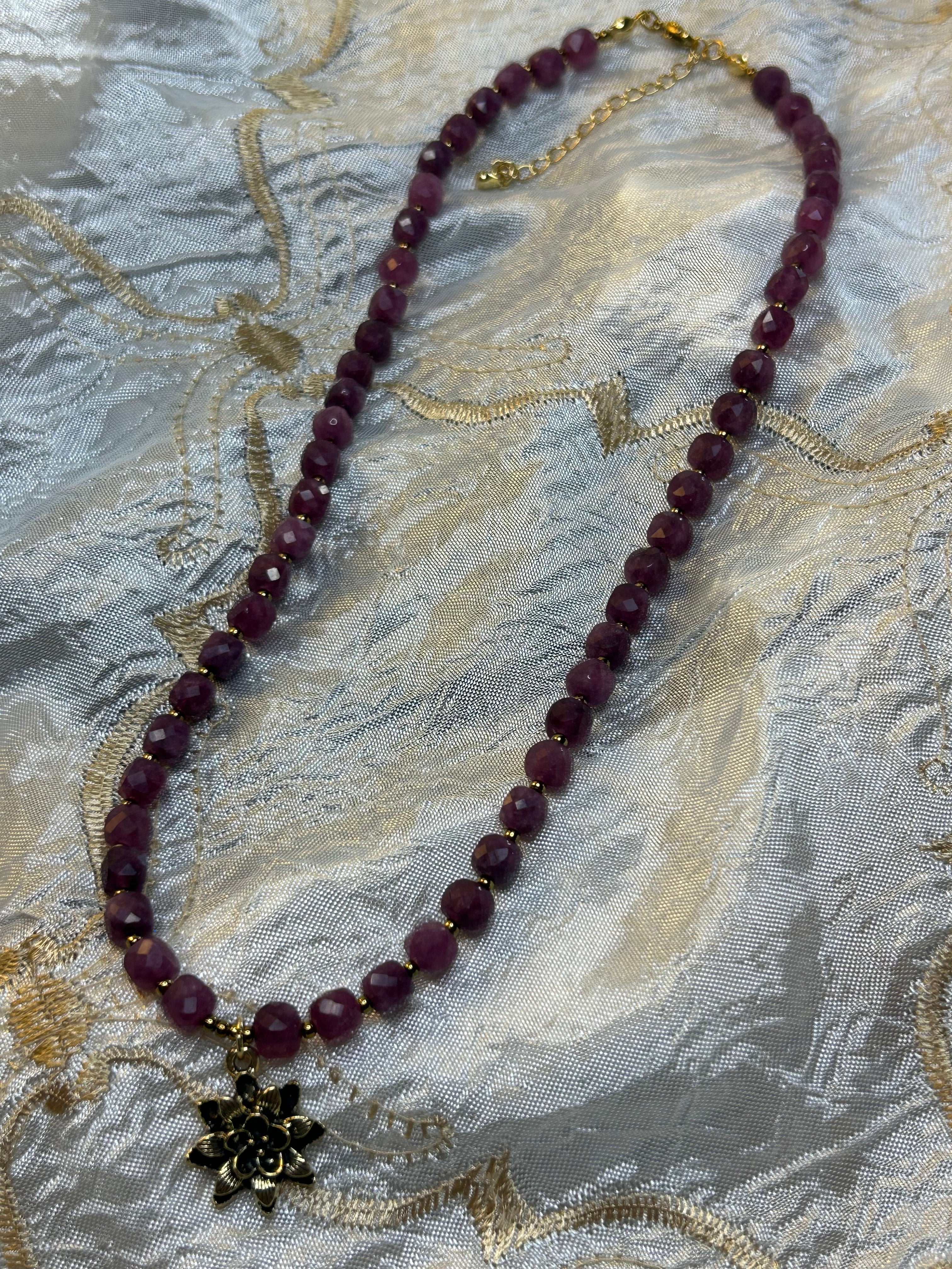 Purple beaded necklace with a gold chain on a textured fabric background