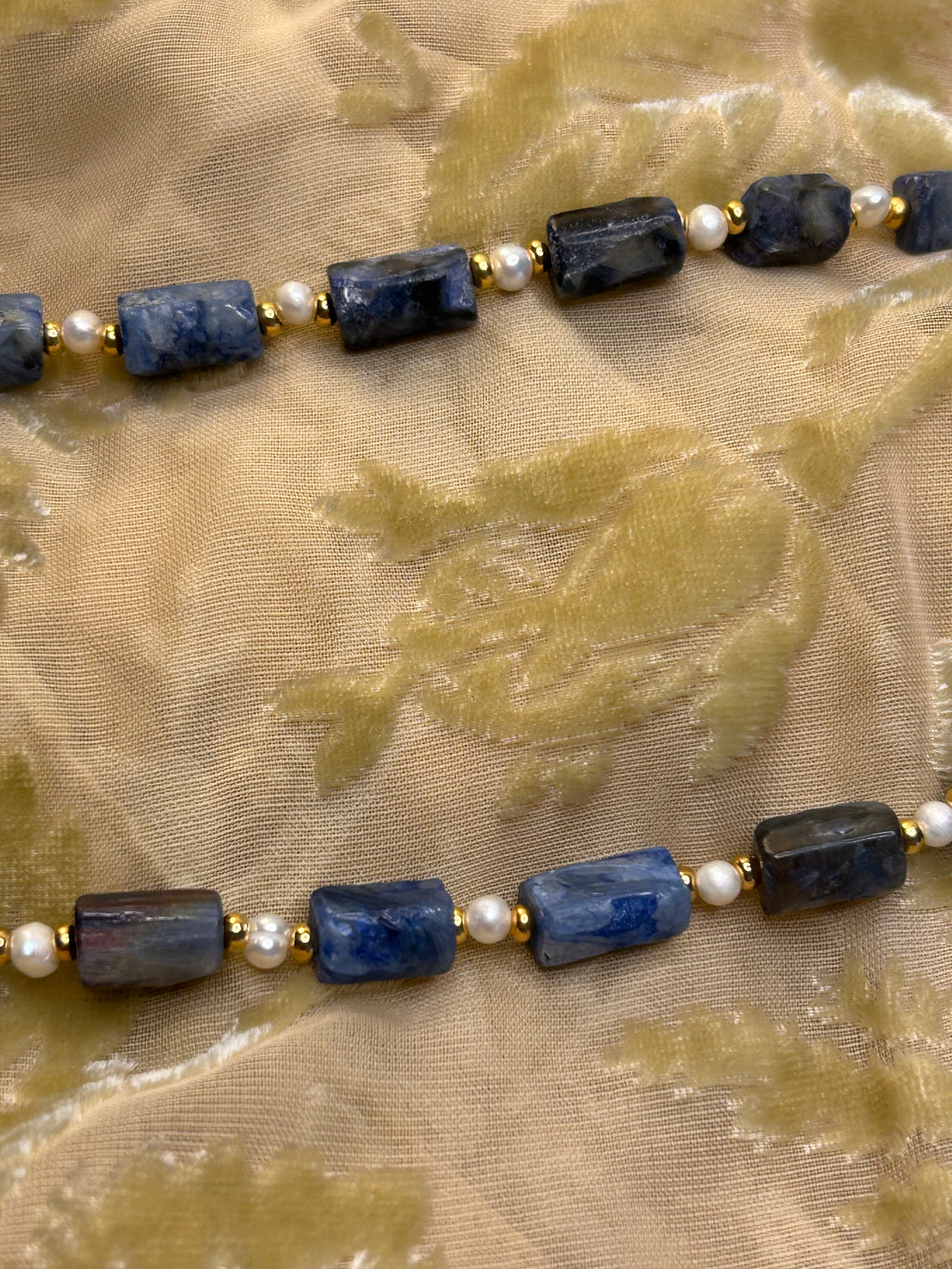 Necklace with blue beads and pearls on a textured beige background
