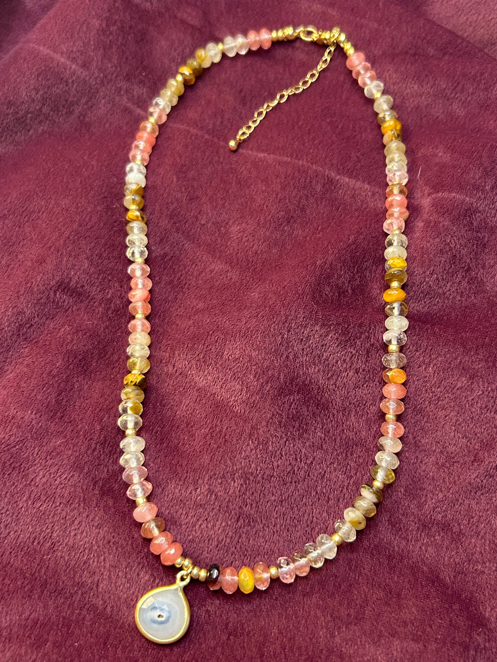 Necklace with multicolored beads and a round pendant on a purple fabric background