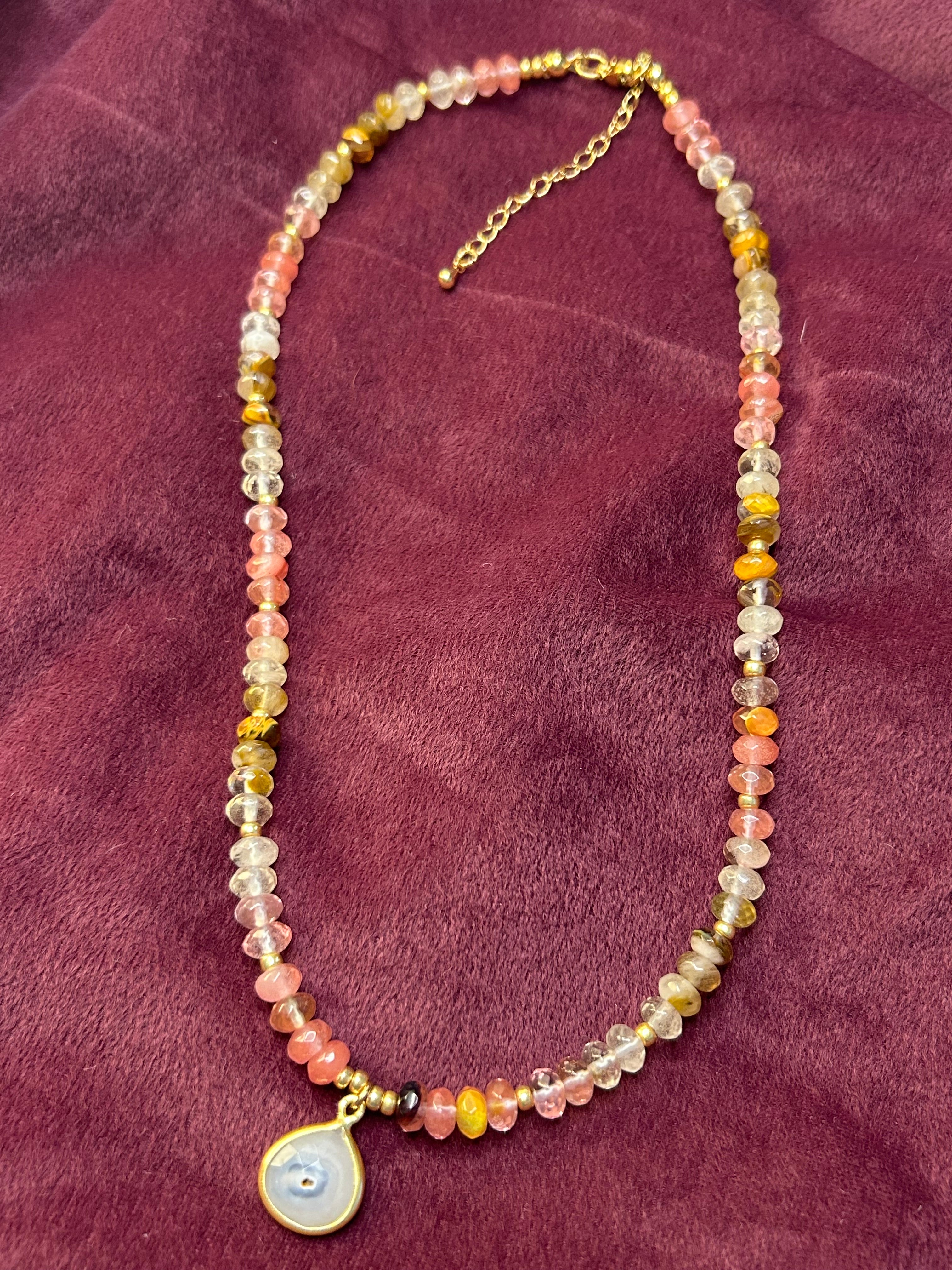 Necklace with multicolored beads and a round pendant on a purple fabric background