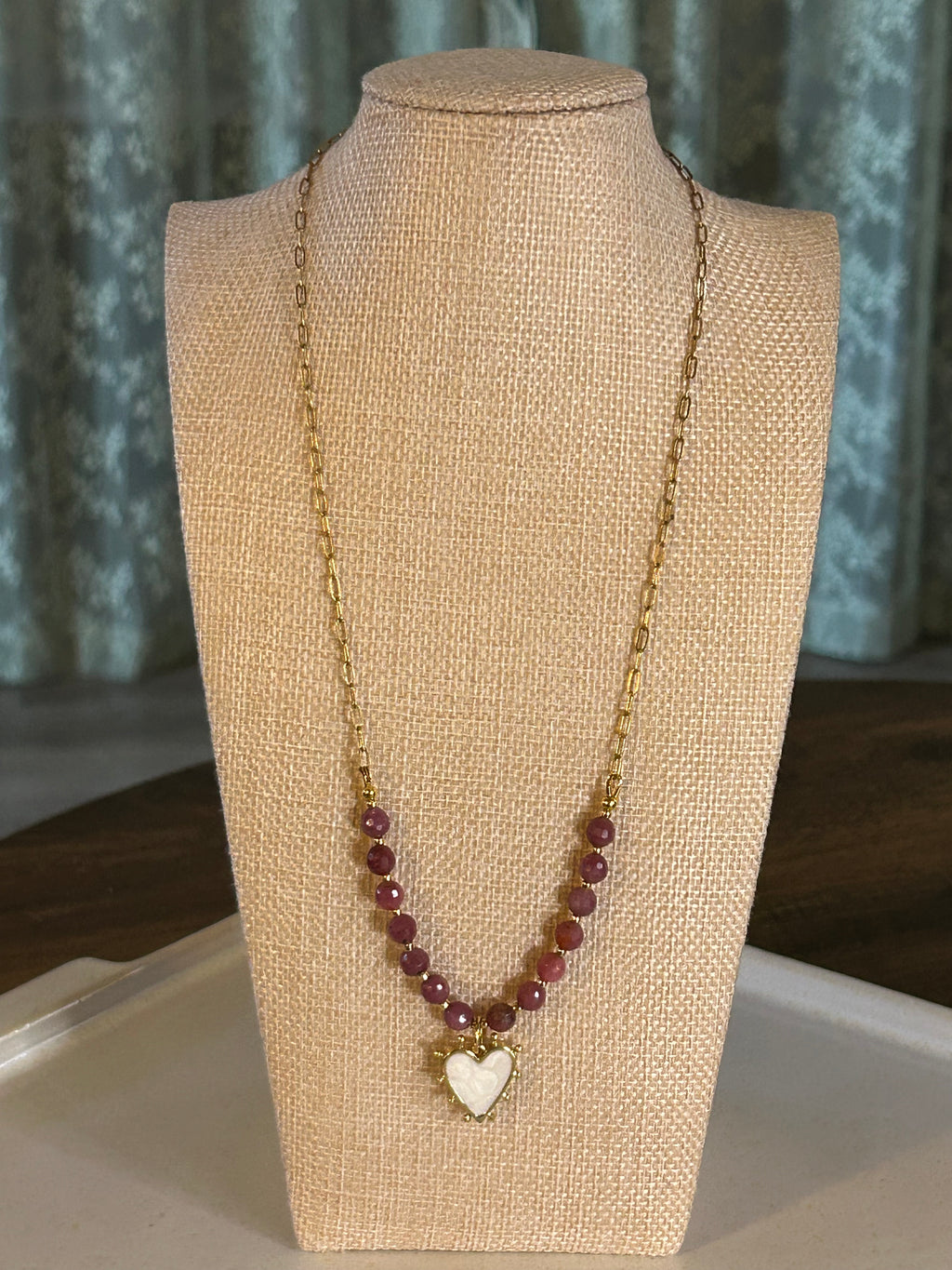Necklace with red beads and a heart charm on a beige mannequin bust.
