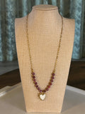 Necklace with red beads and a heart charm on a beige mannequin bust.
