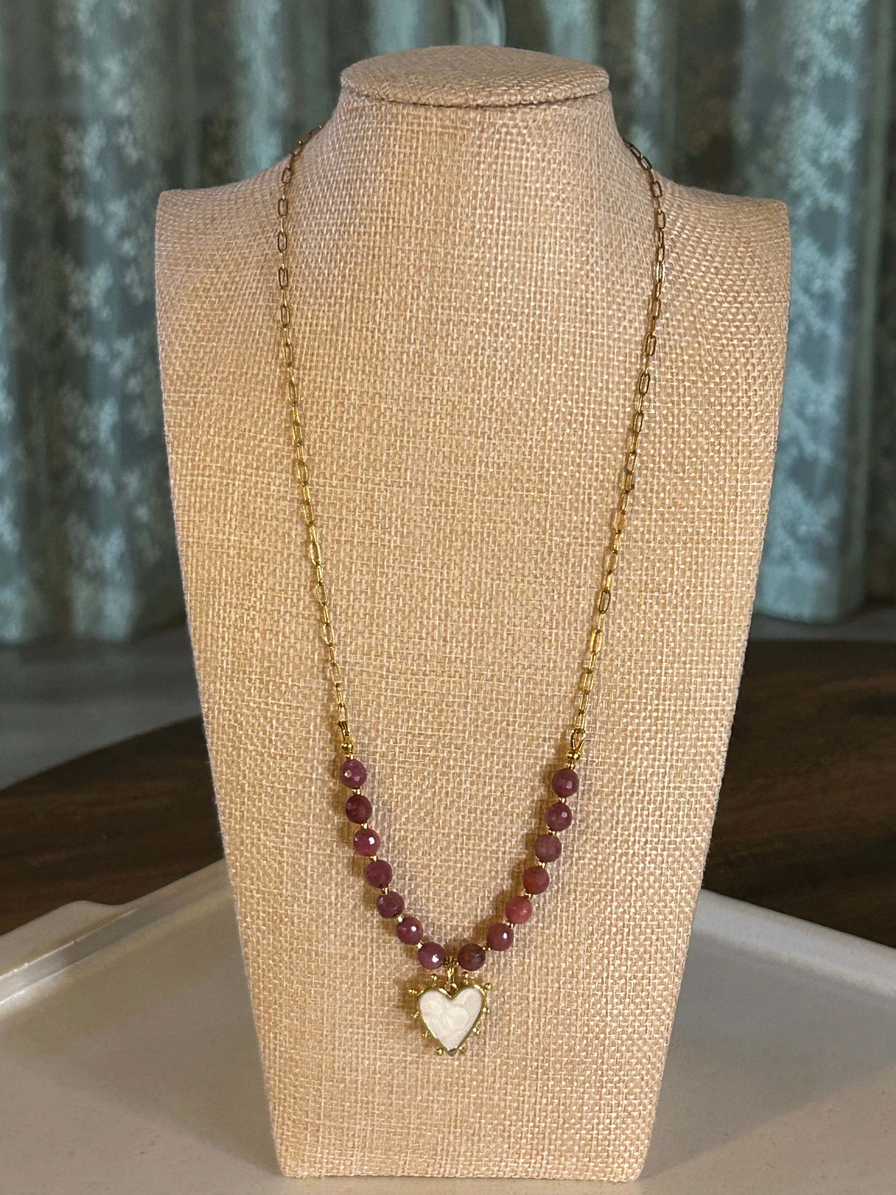 Necklace with red beads and a heart charm on a beige mannequin bust.