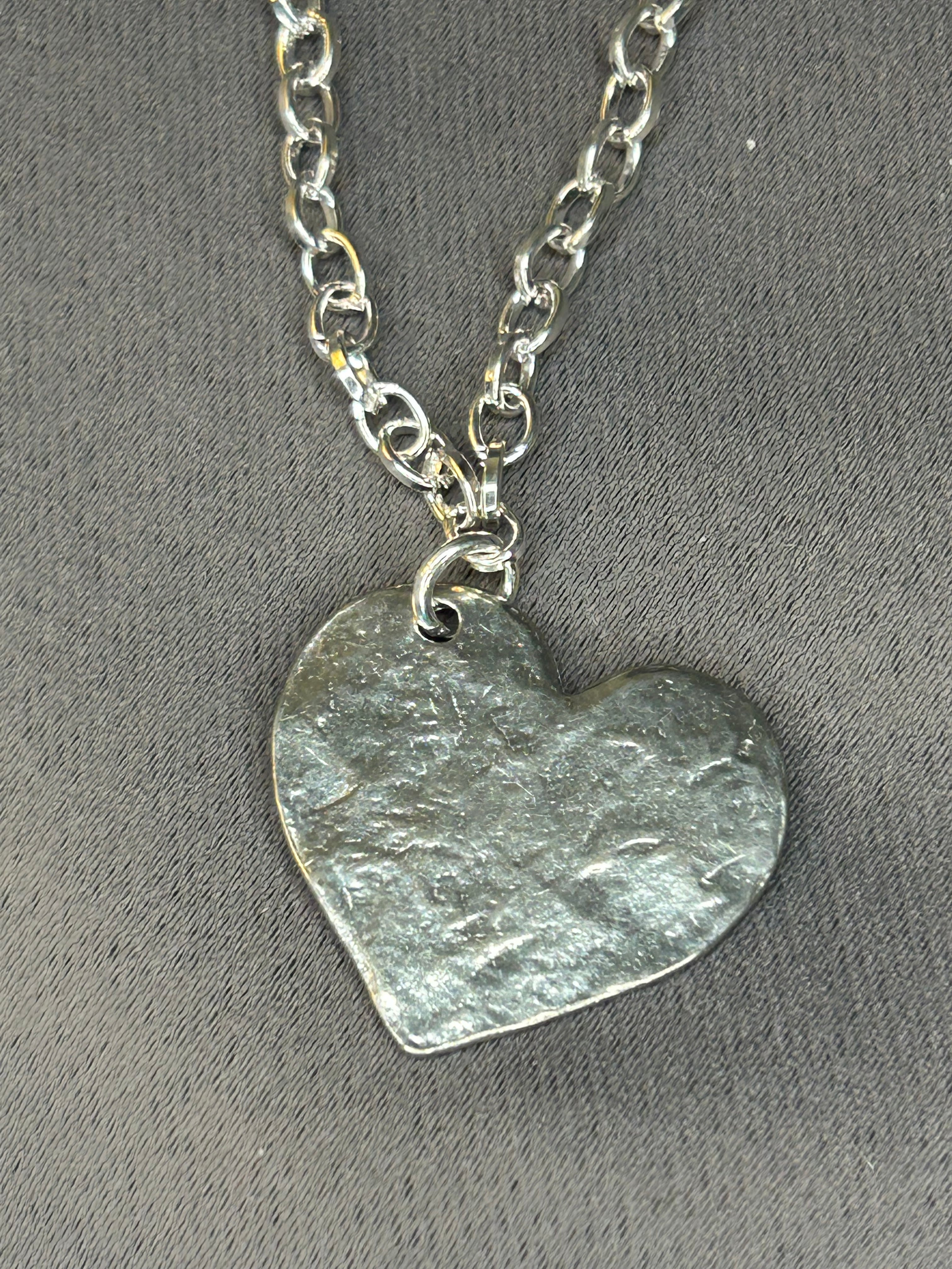 Silver heart-shaped pendant on a chain against a gray background