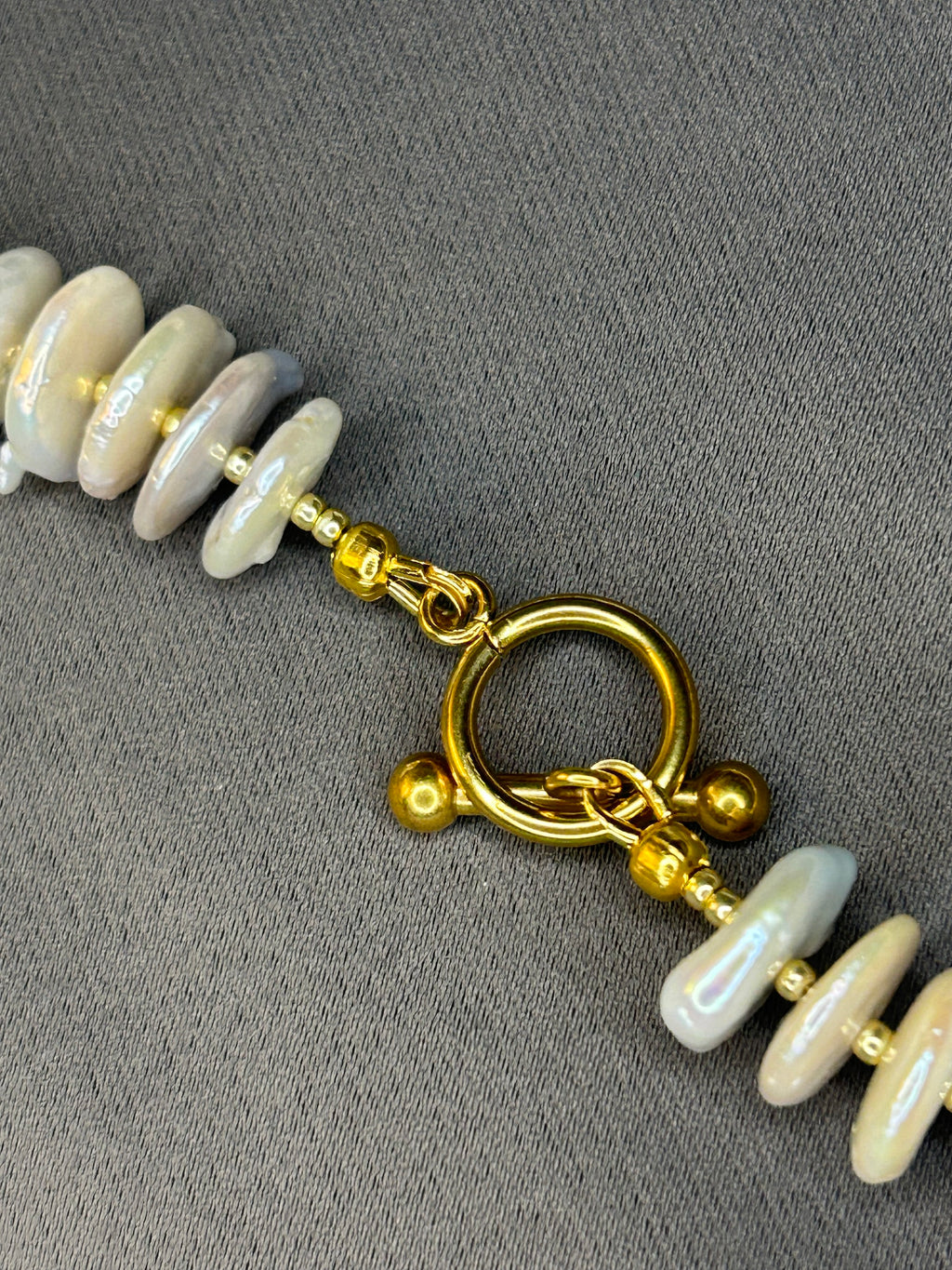 Close-up of a necklace with gold chain and white beads on a gray background