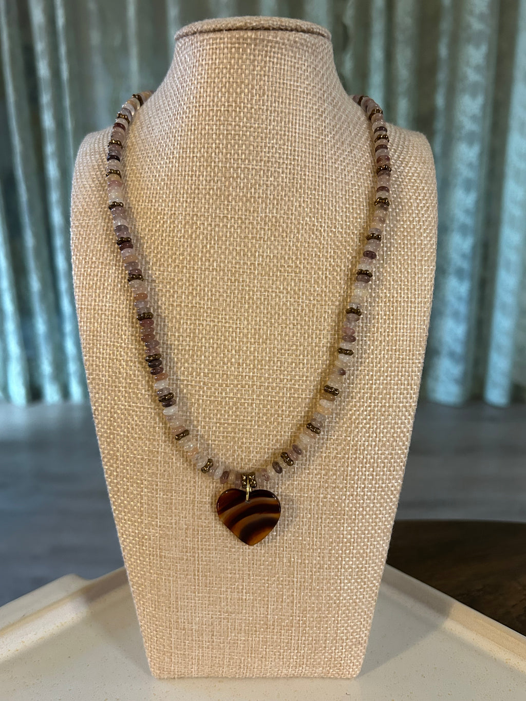 Necklace with a large round pendant on a beige display stand.
