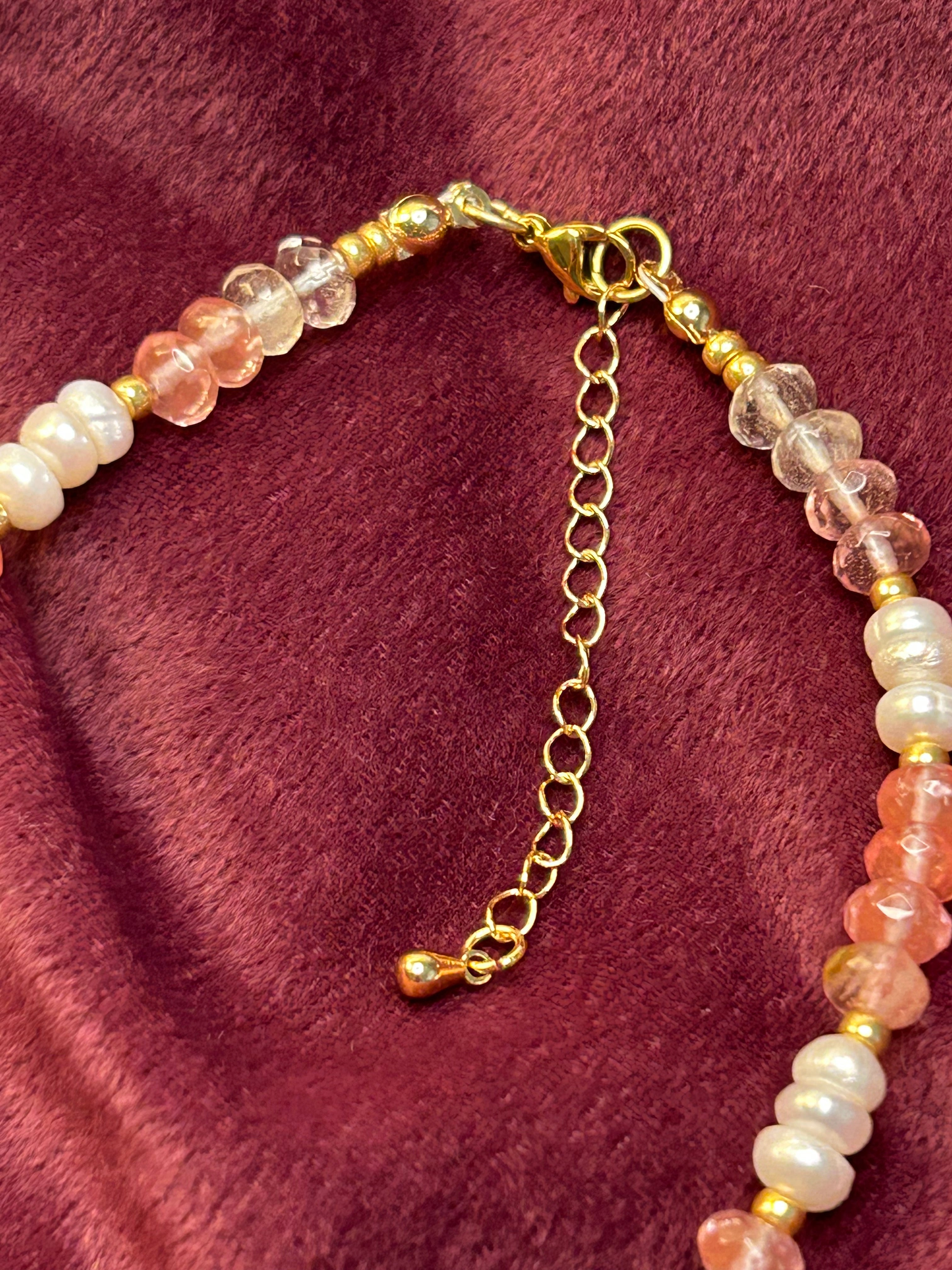 Necklace with pink and gold beads on a maroon fabric background