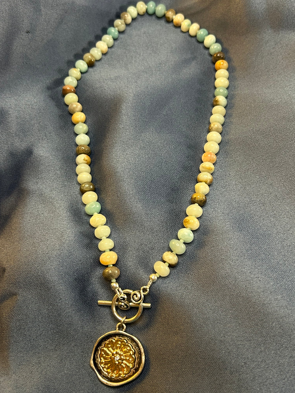 Beaded necklace with a gold pendant on a gray fabric background