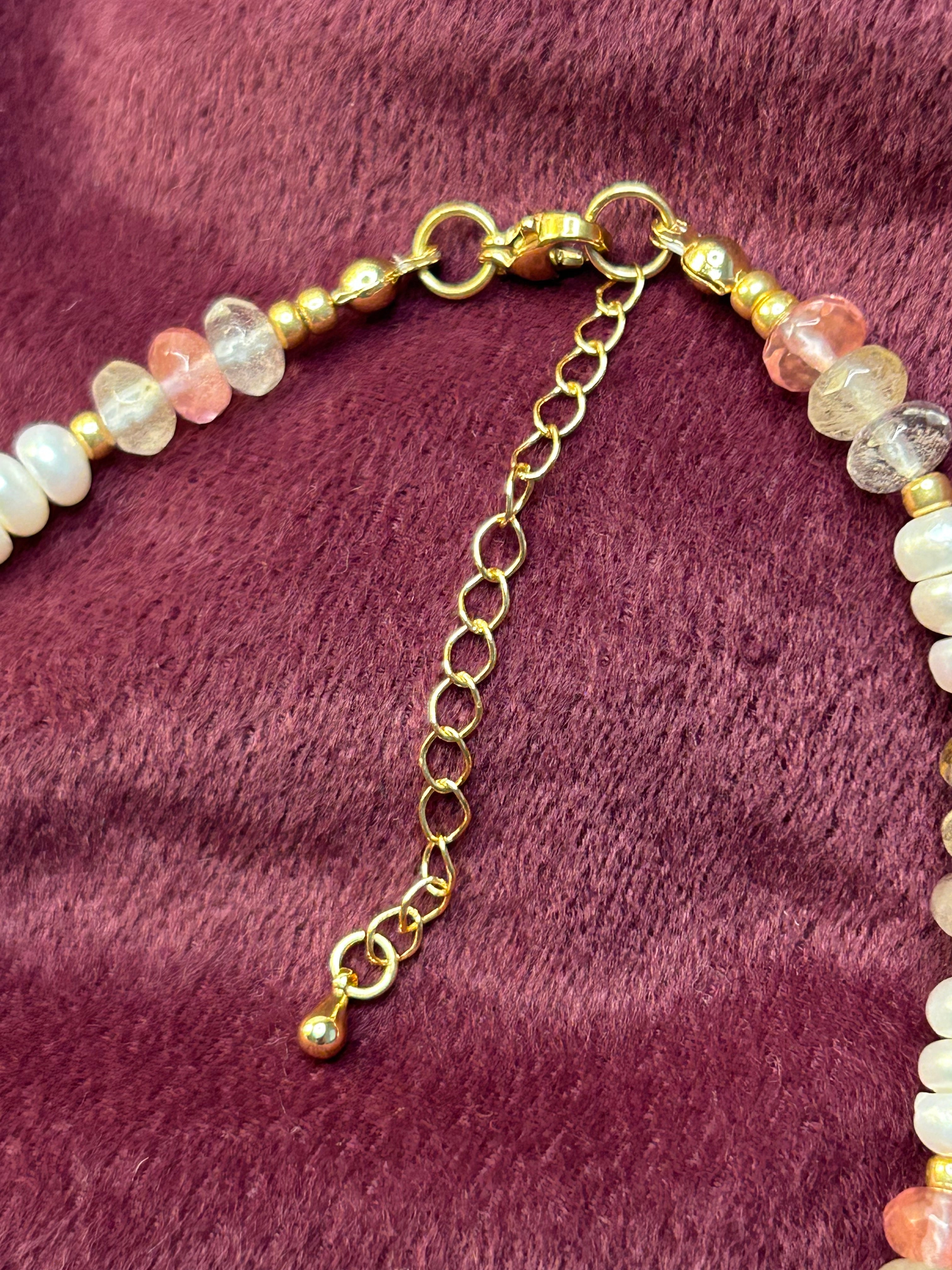 Necklace with multicolored beads and gold chain on a purple fabric background