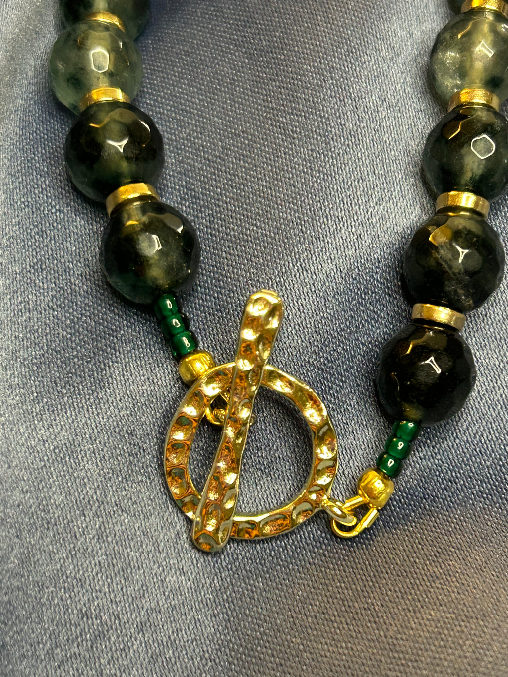 Necklace with green beads and gold clasp on a gray fabric background