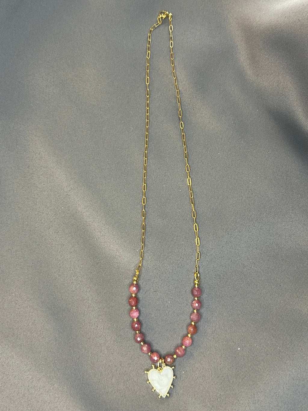 Necklace with pink beads and a heart-shaped pendant on a gray fabric background