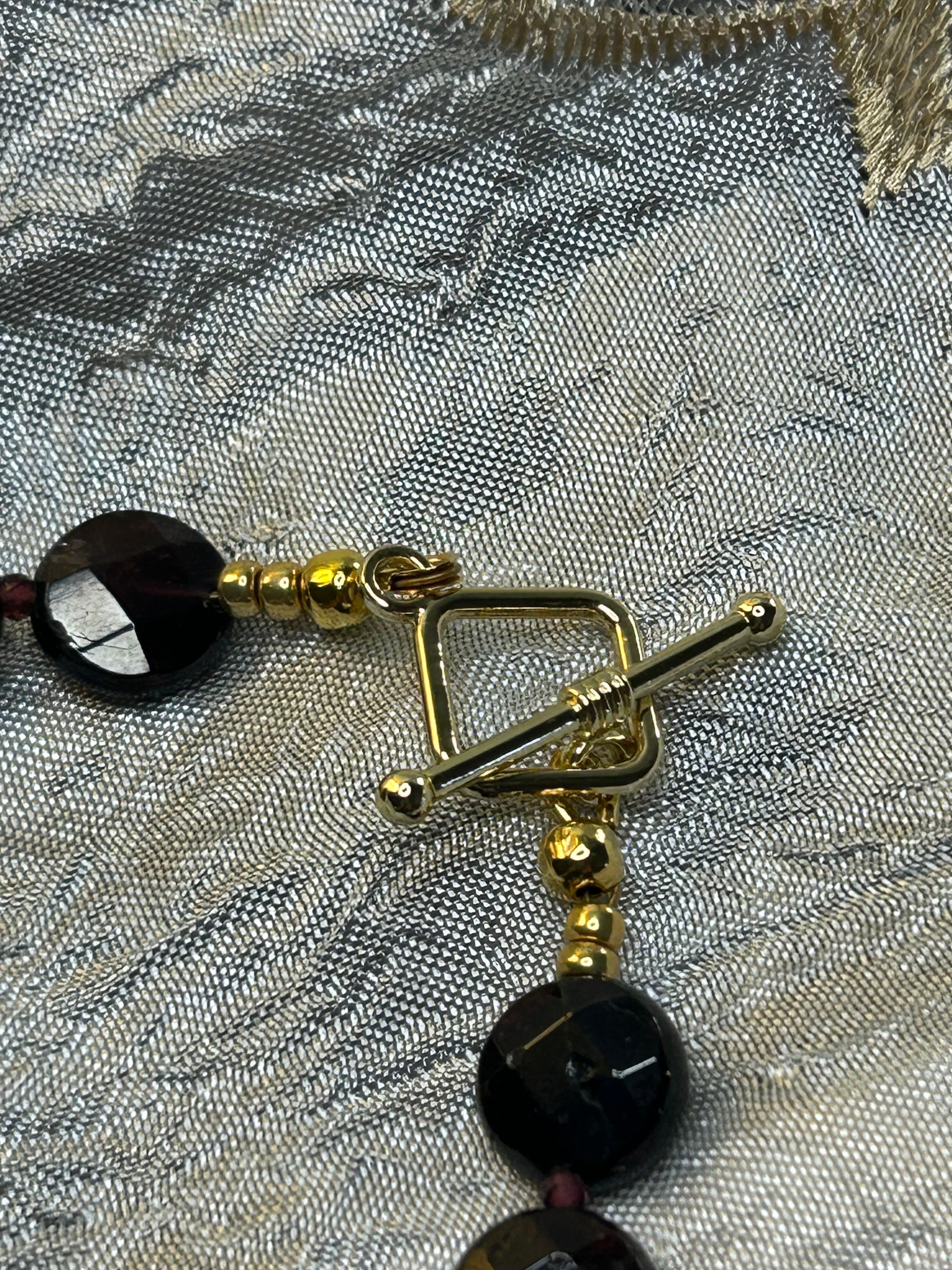 Gold toggle with dark beads on a textured fabric background