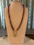 Necklace with red beads and gold clasp on a beige display stand.
