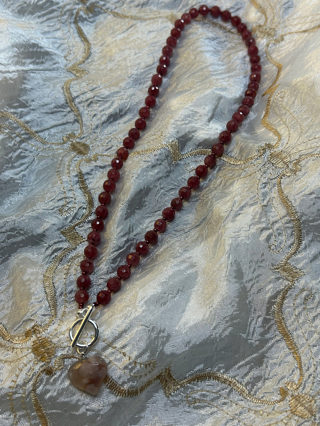 Red beaded necklace with a clasp on an embroidered fabric background