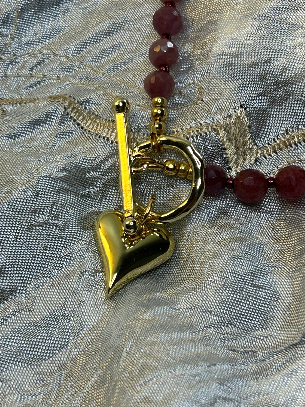 Gold heart charm on a red beaded necklace against a textured gray background