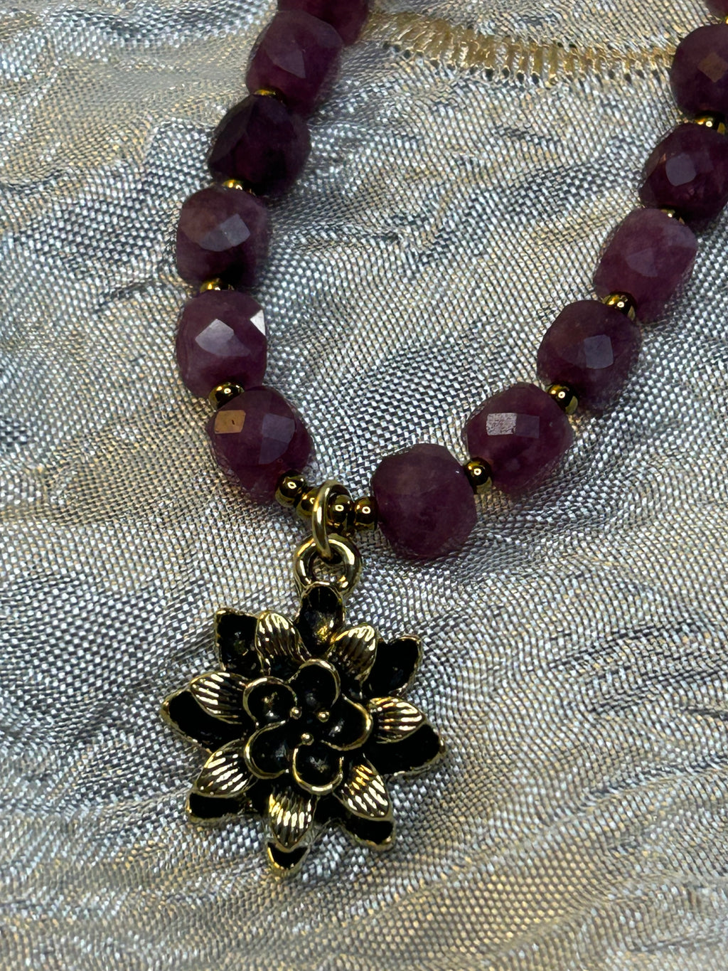 Necklace with purple beads and a gold flower charm on a textured fabric background