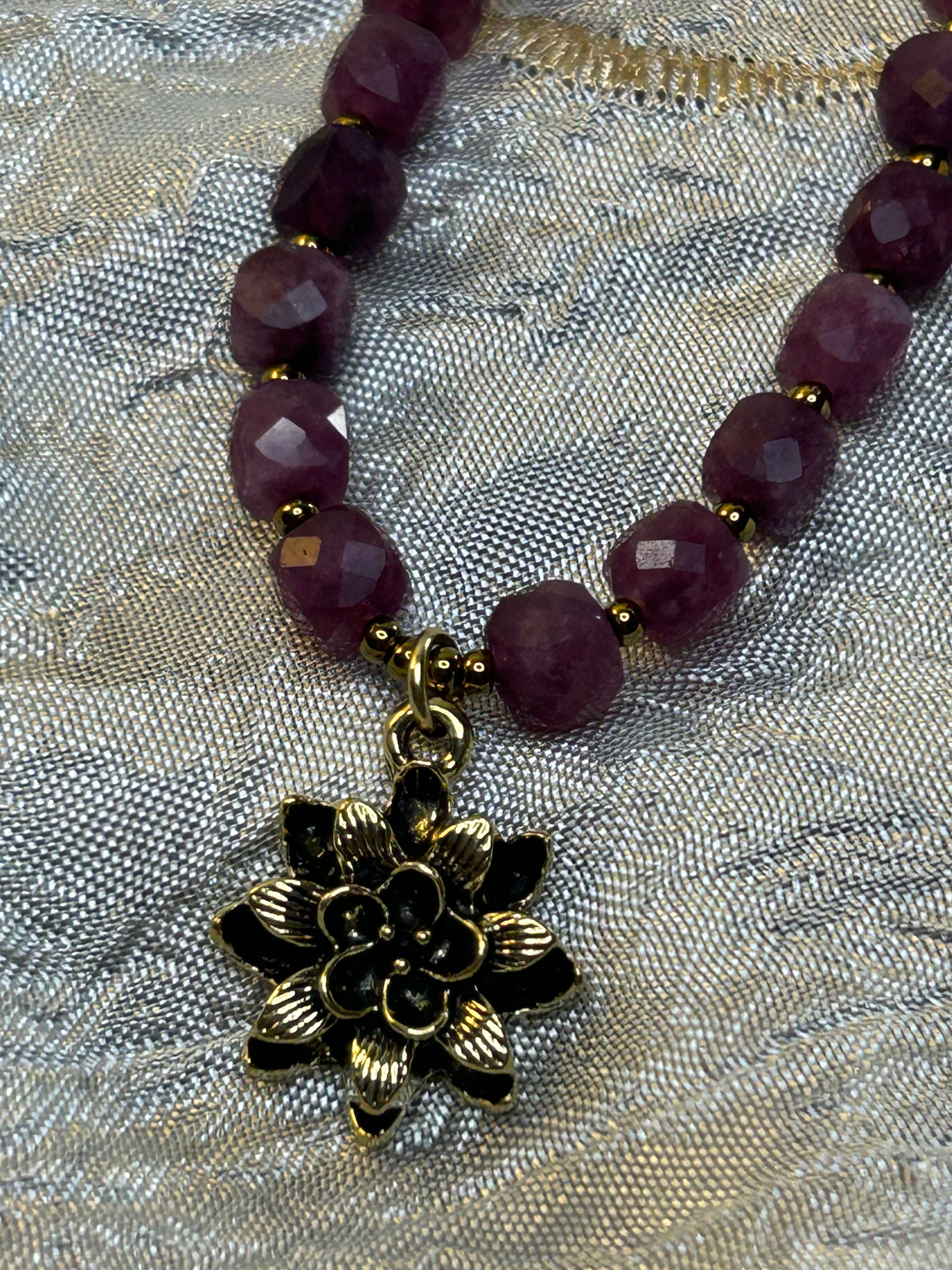 Necklace with purple beads and a gold flower charm on a textured fabric background