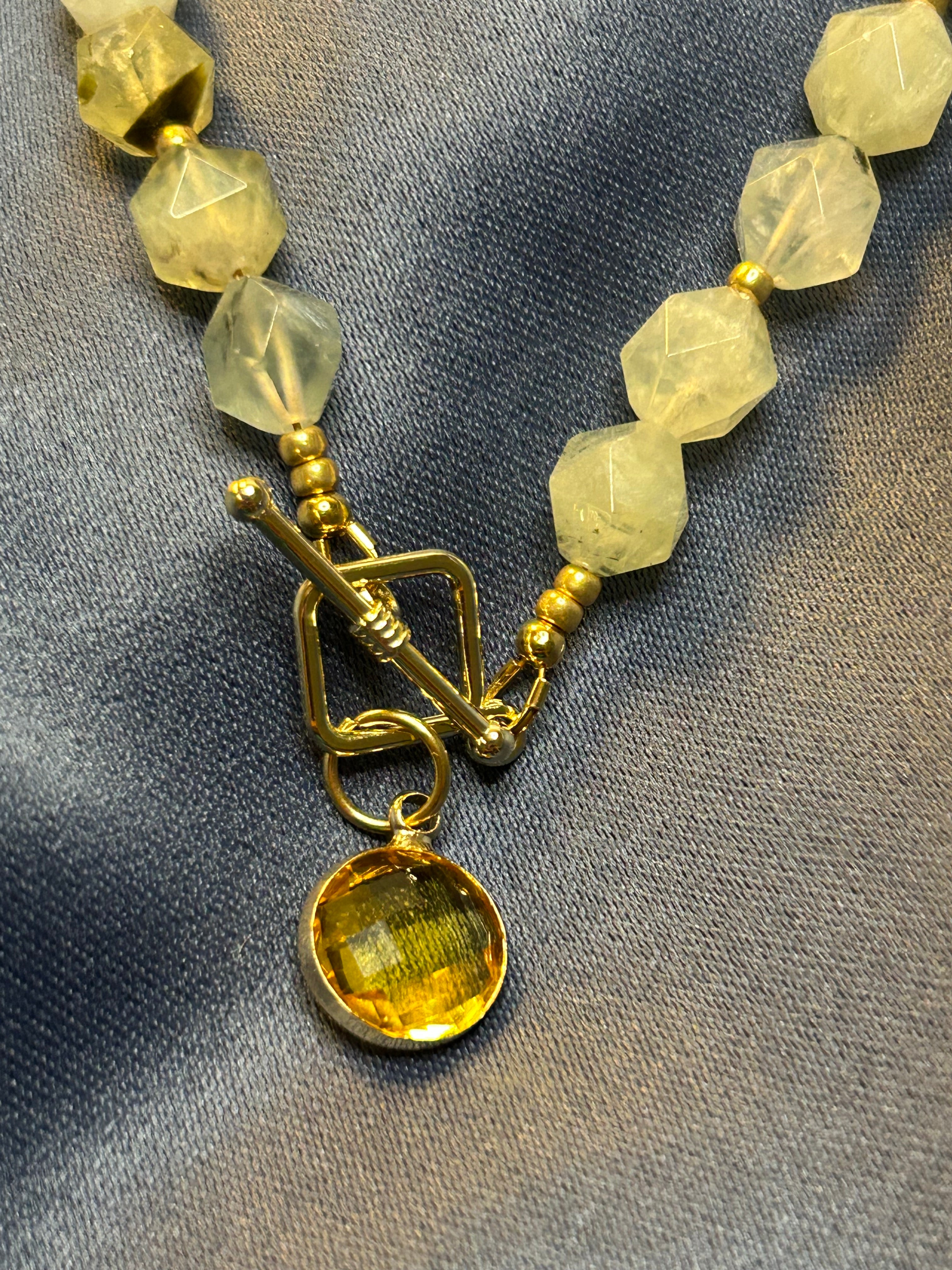 Necklace with green-yellow beads and gold charm on a gray fabric background
