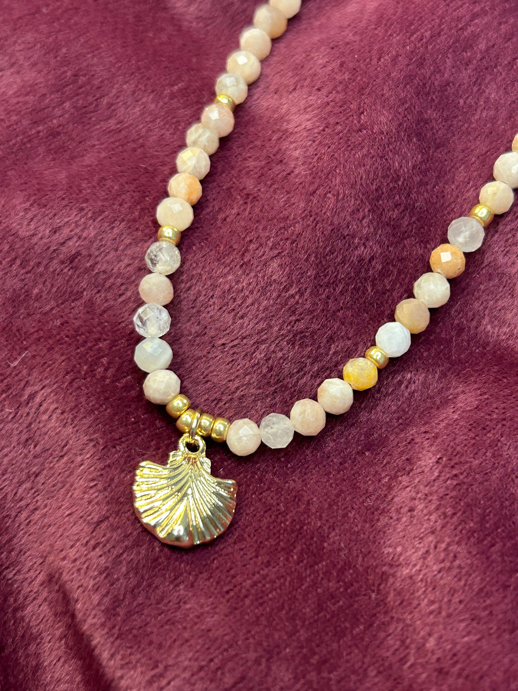 Beaded necklace with a shell charm on a purple fabric background