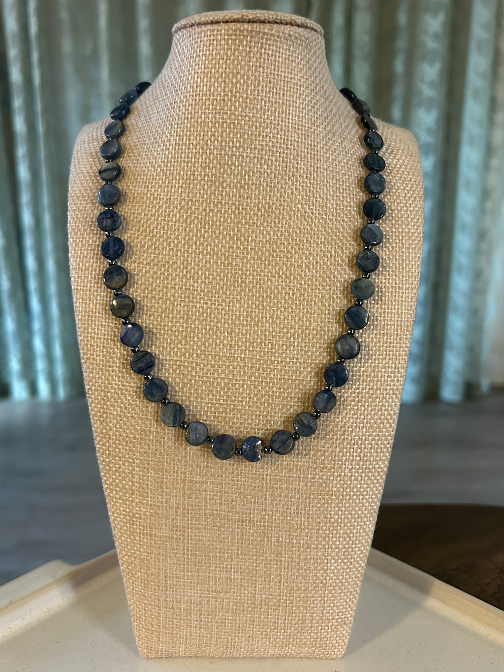 Black and blue beaded necklace on a beige jewelry display