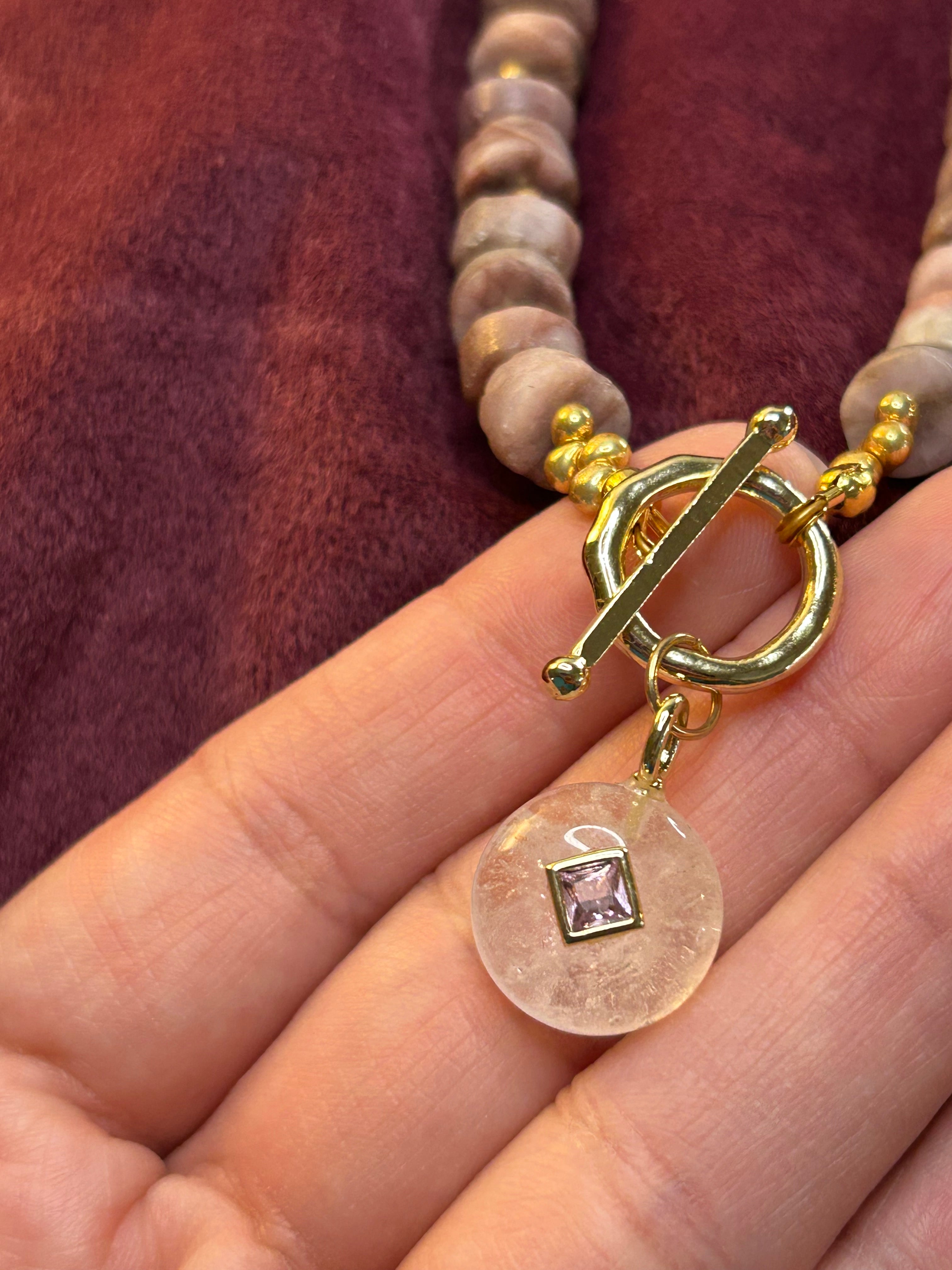 Close-up of a hand holding a beaded bracelet with a gold clasp and pink gemstone.