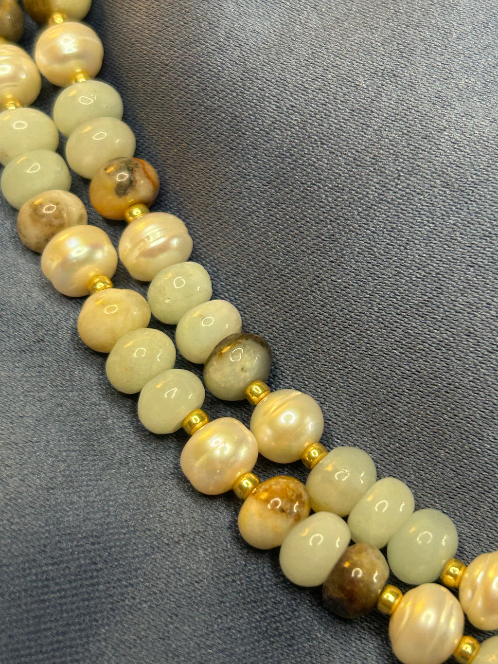 Necklace with light-colored beads and gold accents on a gray fabric background