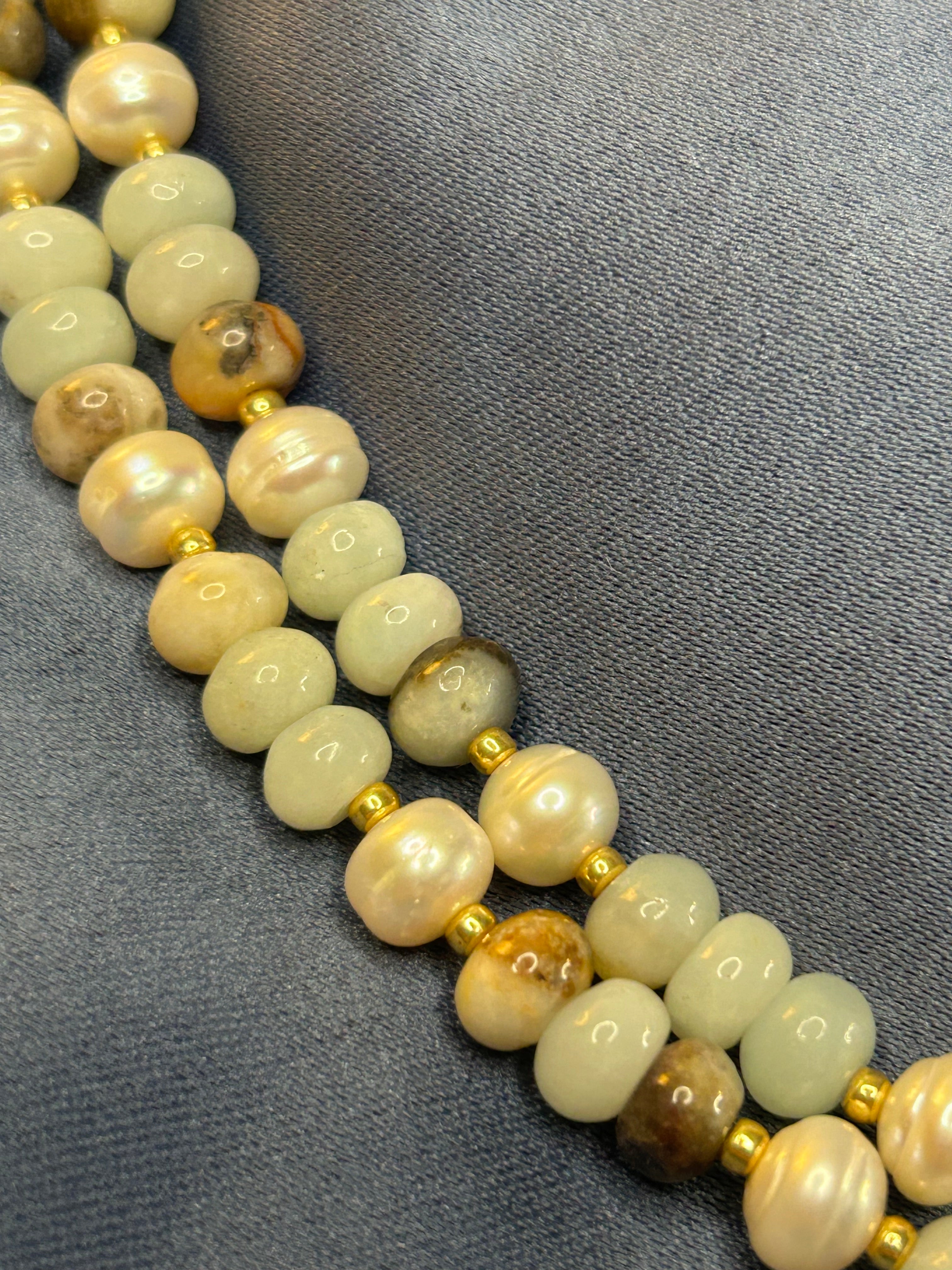 Necklace with light-colored beads and gold accents on a gray fabric background
